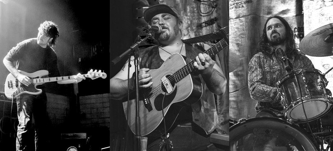 Three musicians performing on stage: a guitarist on the left, a singer with a guitar in the center, and a drummer on the right.