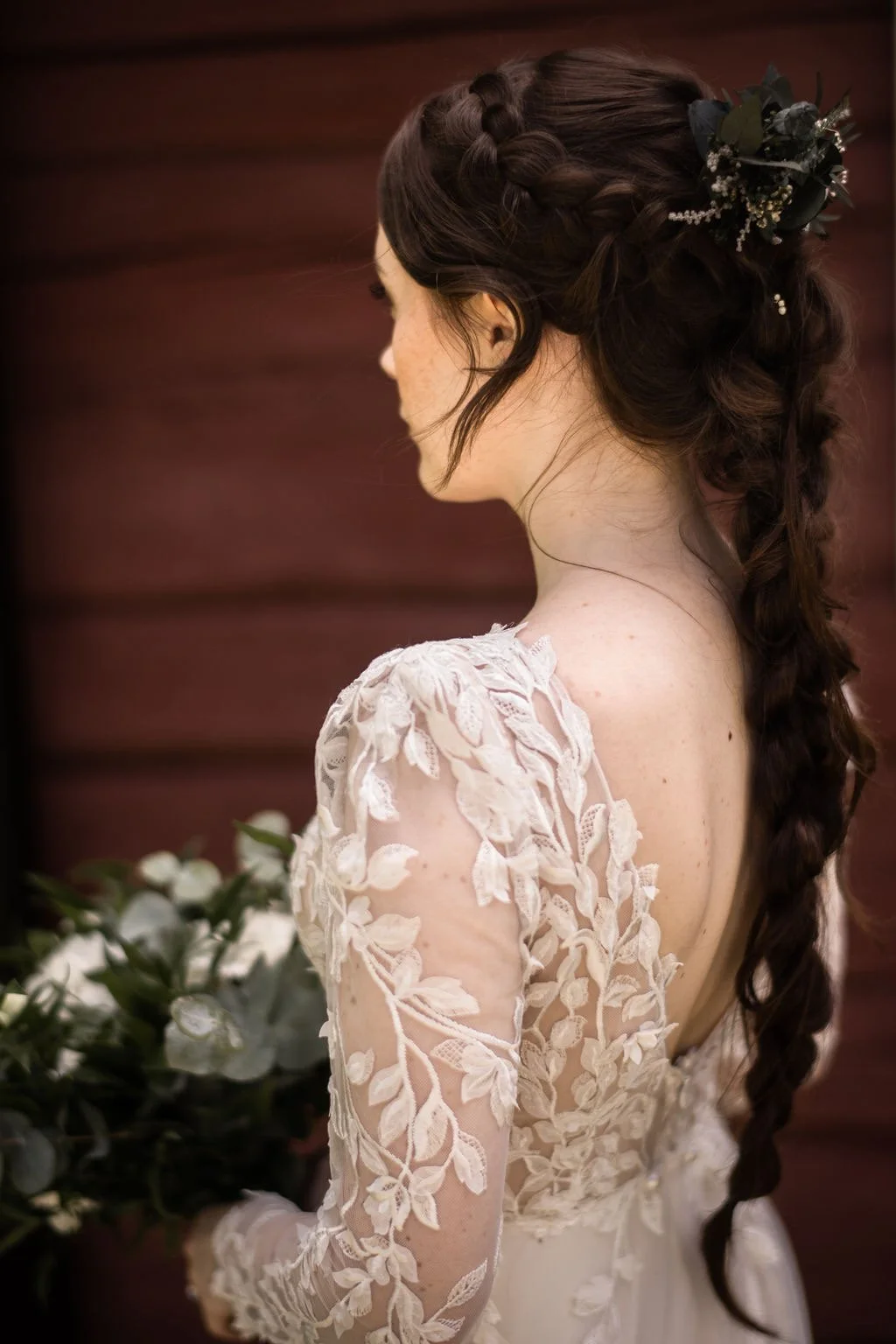 Häämeikki ja kampaus kuvattuna morsiamella punamullalla maalattujen hirsien edessä