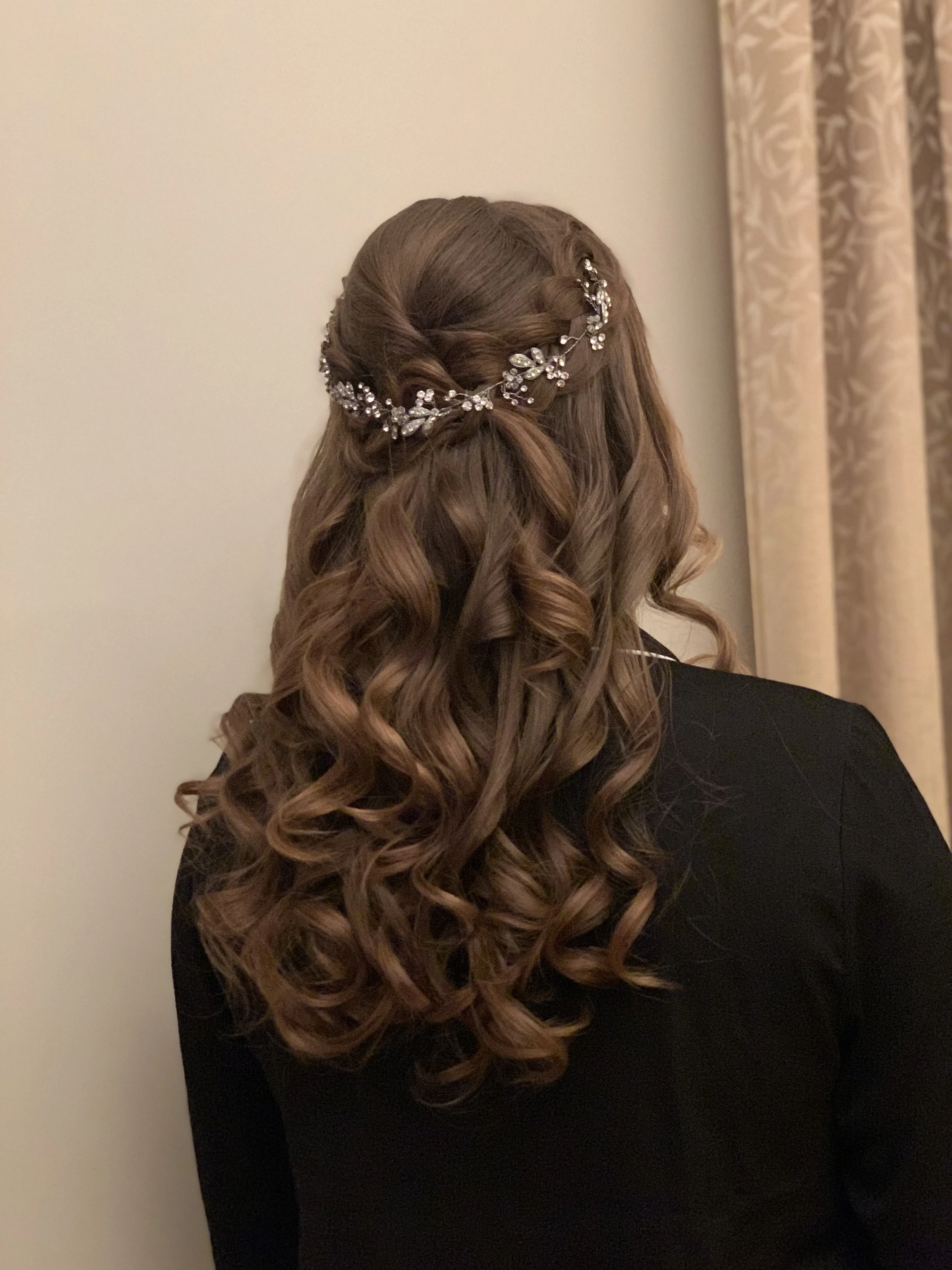 Kiharakampaus / hääkampaus pitkissä tummissa hiuksissa, joissa hiuskoriste. Kuvattu juhlapaikalla Helsingissä. 