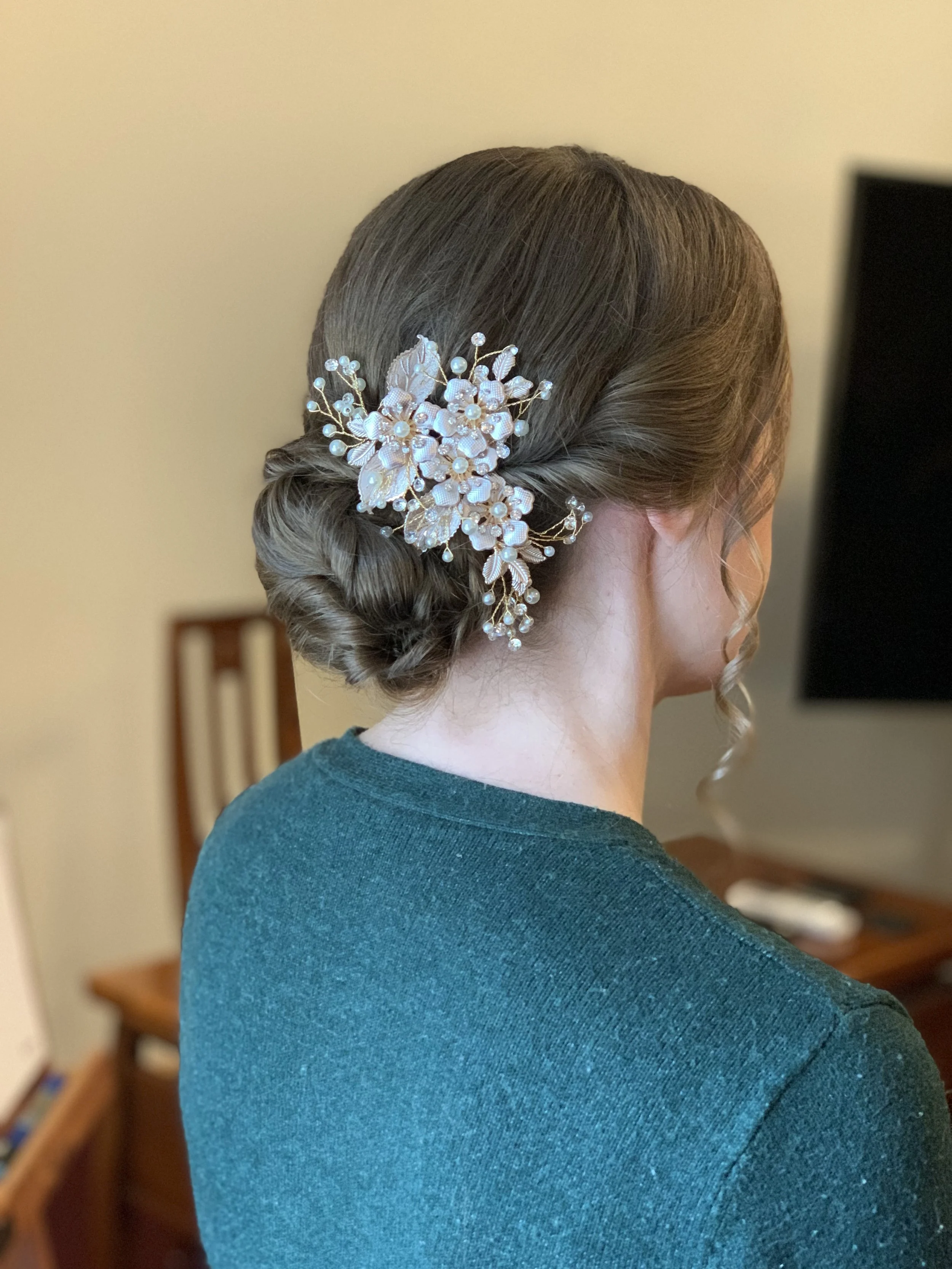 Kampaajan tekemä juhlakampaus hiuskoristeella tummissa hiuksissa