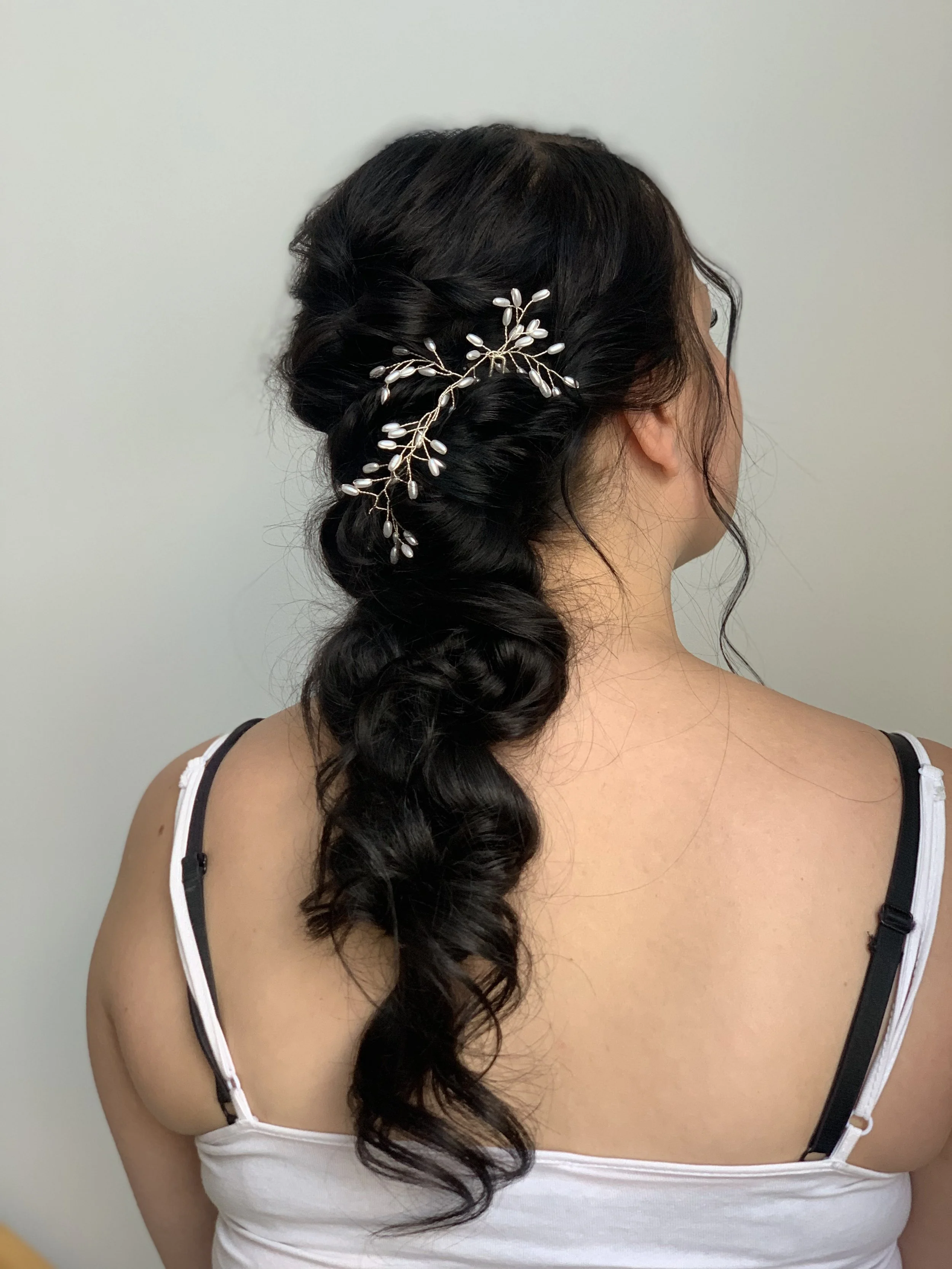 Kampaajan tekemä hääkampaus jossa tummissa pitkissä hiuksissa kiharoita ja koriste