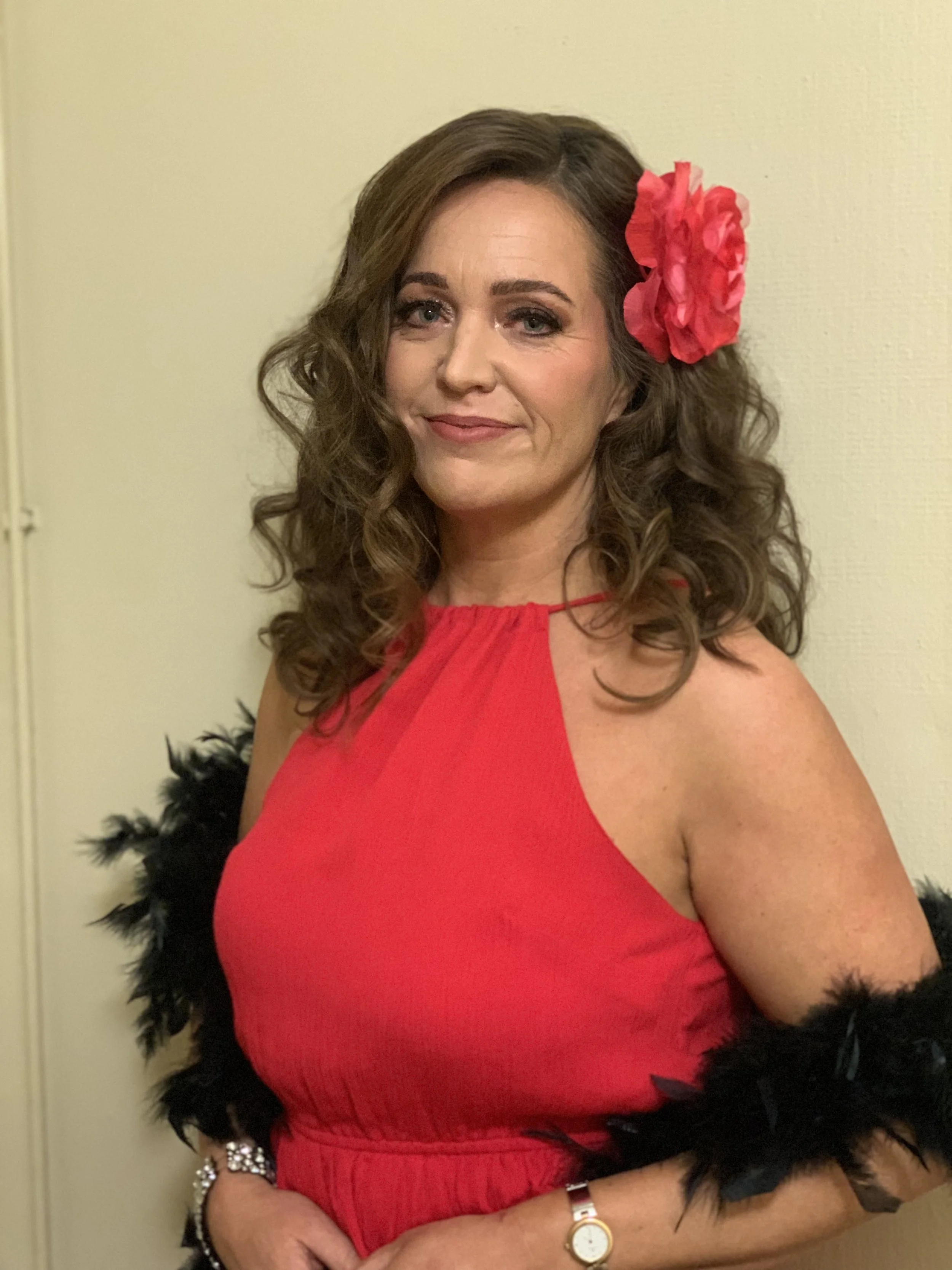 Juhlameikki ja kampaus tummahiuksisella naisella jolla punainen kukka hiuksissa ja punainen mekko päällä