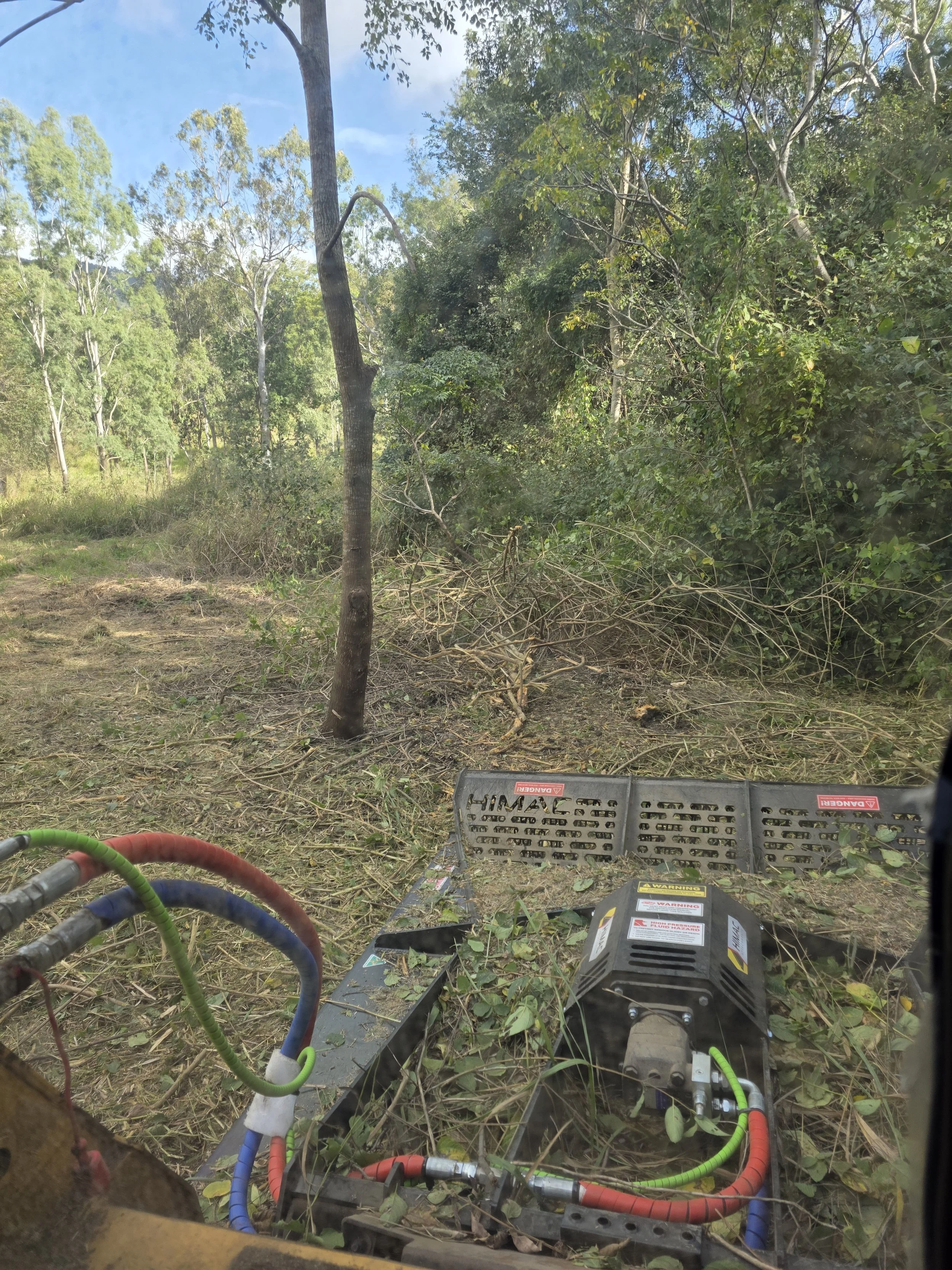 View from inside forestry equipment showing electrical cables and devices on the ground with trees and blue sky in the background.