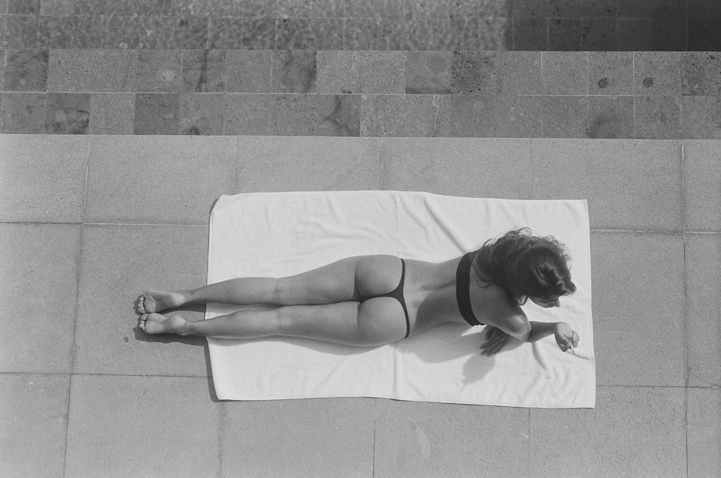 A woman lying on her stomach on a white towel on a tiled surface, facing downward.
