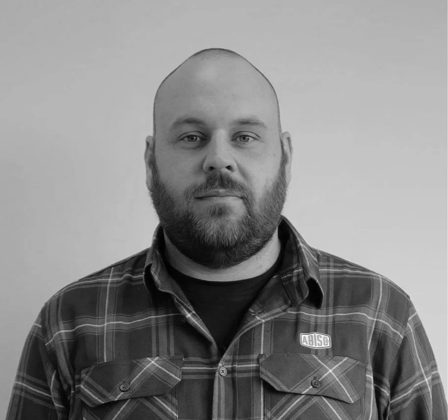 Black and white portrait of a man with a beard, wearing a plaid shirt, facing the camera with a neutral expression.