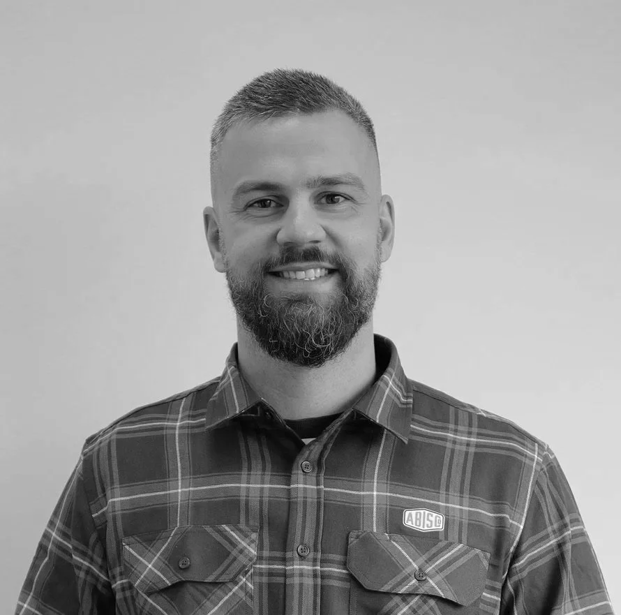 Black and white portrait of a man with short hair and a beard, smiling, wearing a plaid shirt.