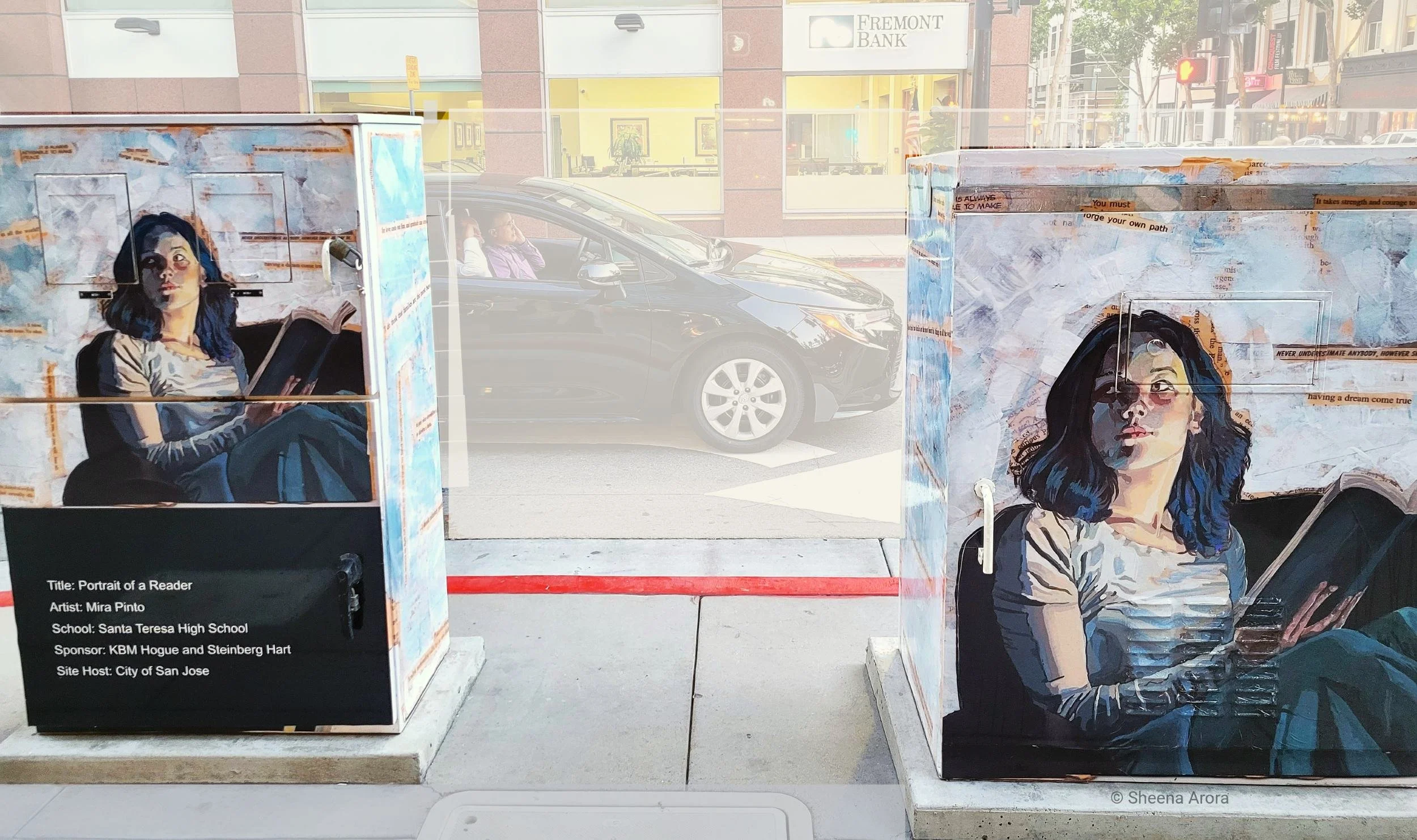 Outdoor street art on a utility box by Mira Pinto depicting a young woman sitting in a dark chair reading an open book. The artwork features a collaged, paper-textured background with painted text fragments, warm cream highlights, and soft blue tones