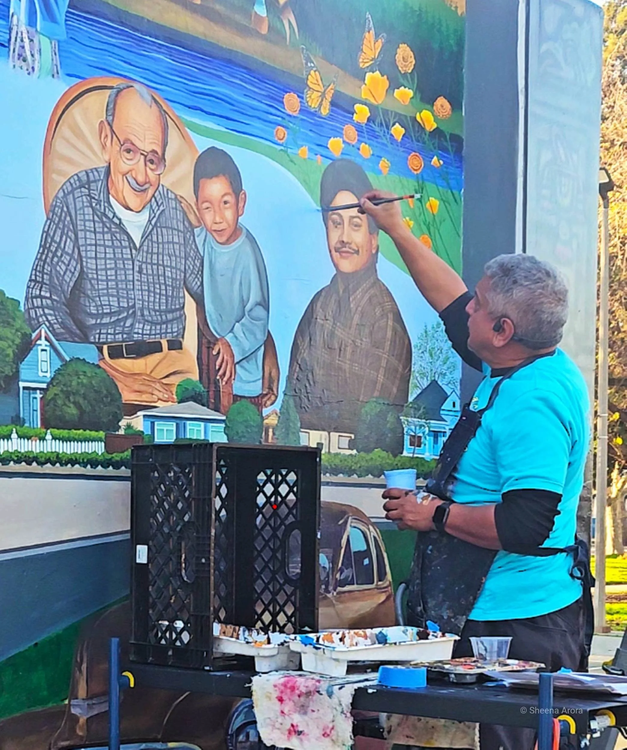 Artist Alfonso Salazar adding detailed paintbrush strokes to a Chicano community mural in San José, illustrating the living, fragile nature of urban street art described by Sheena Arora.