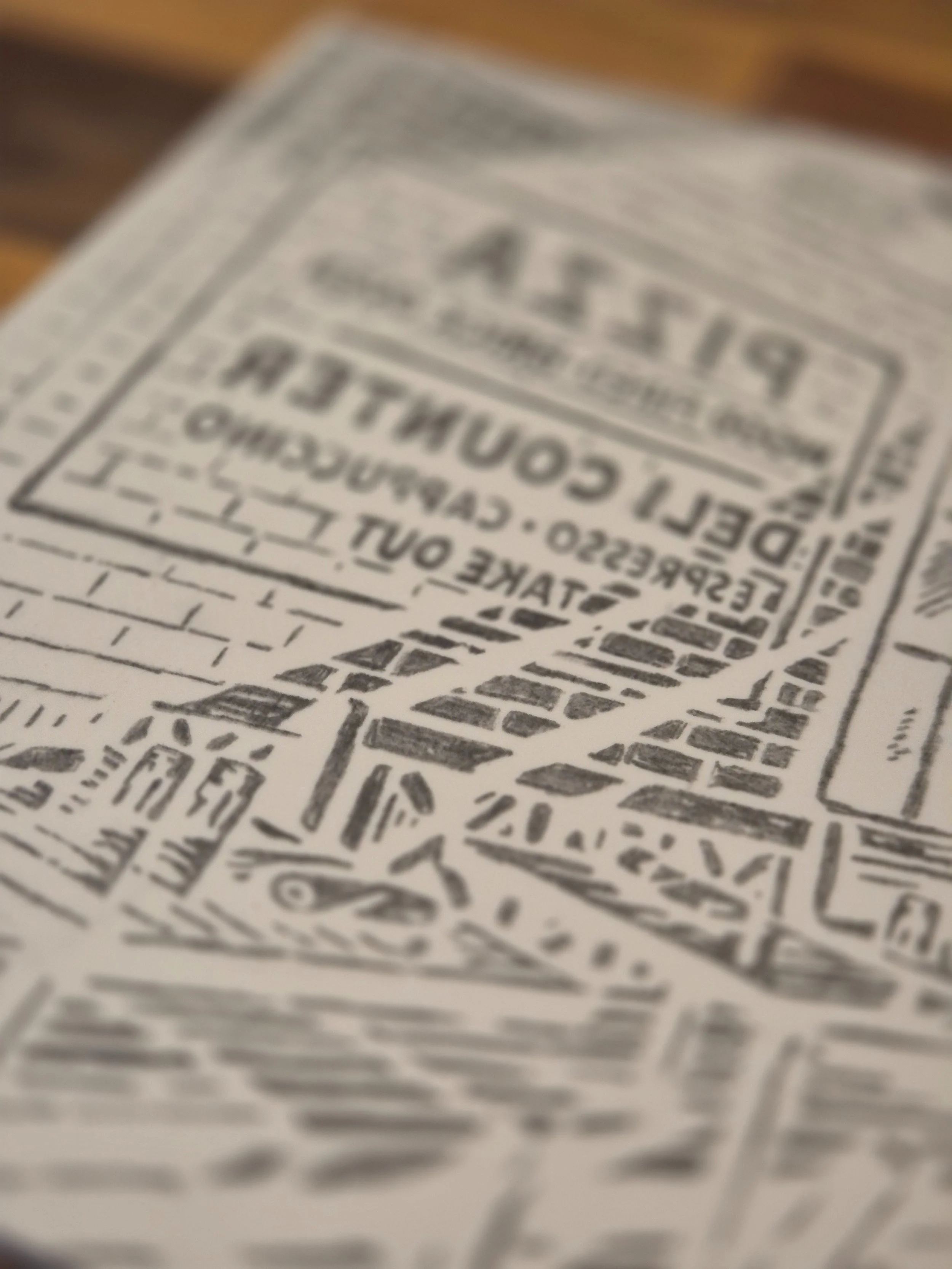 Gros plan sur la plaque de linogravure « Caffè all’Angolo » – détails des lettres, briques et enseignes de pizzeria, art imprimé en linogravure montrant les textures gravées à la main.