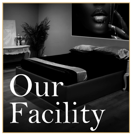 A black and white photo of a bedroom with a bed, pillows, a side table with decorative items, a large plant, and a framed art piece of a woman's face on the wall. The text "Our Facility" is written at the bottom.