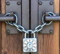 A metal padlock securing a door with a chain, attached to a wooden surface.