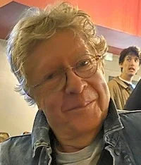 Smiling AI Tamer Rod, hirsute blond, wearing glasses and a denim trucker's jacket.