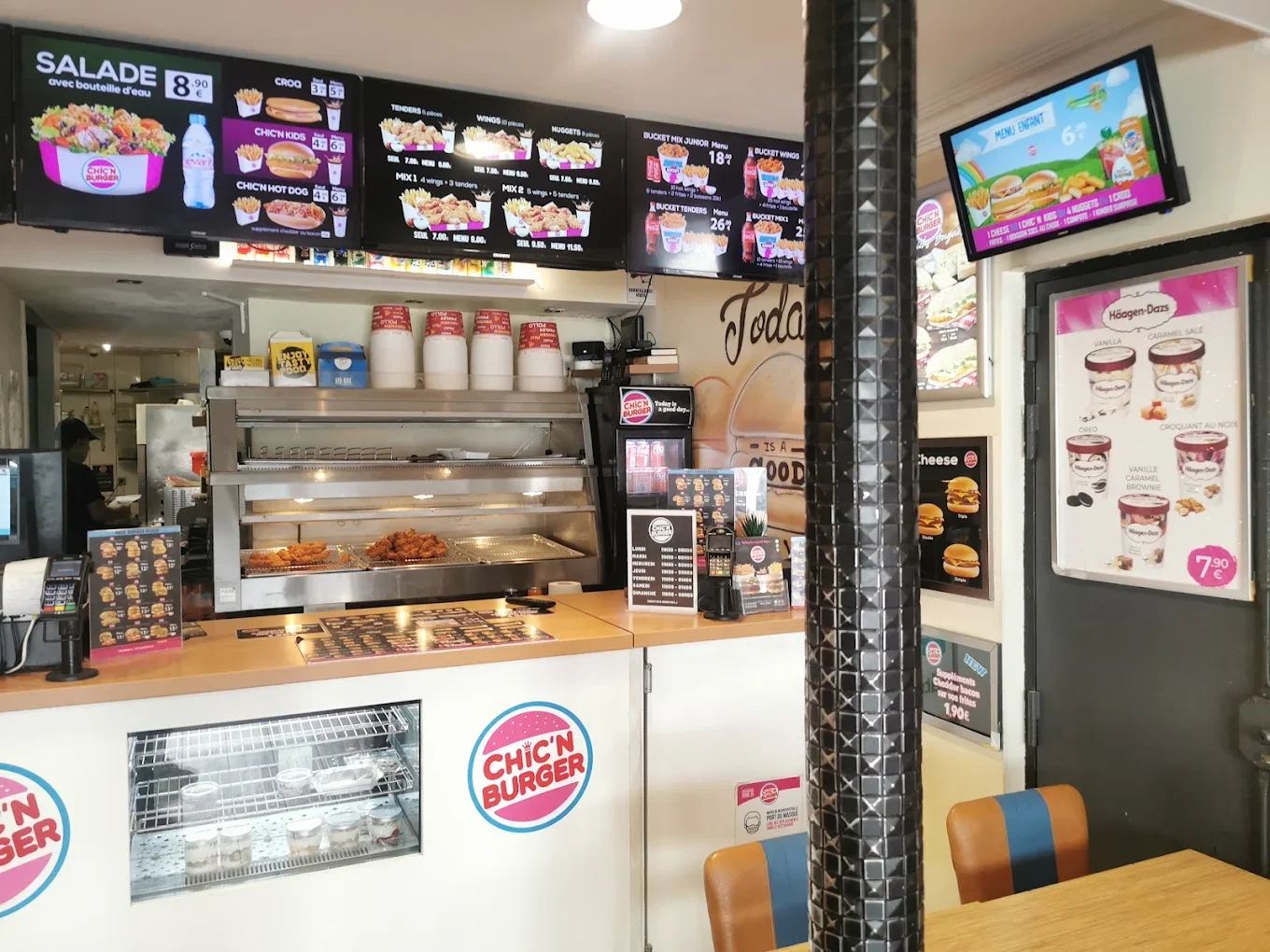 Intérieur d'un fast-food Chick'n Burger avec menu affiché à l'écran, comptoir avec nourriture friture, et posters de glaces Häagen-Dazs.