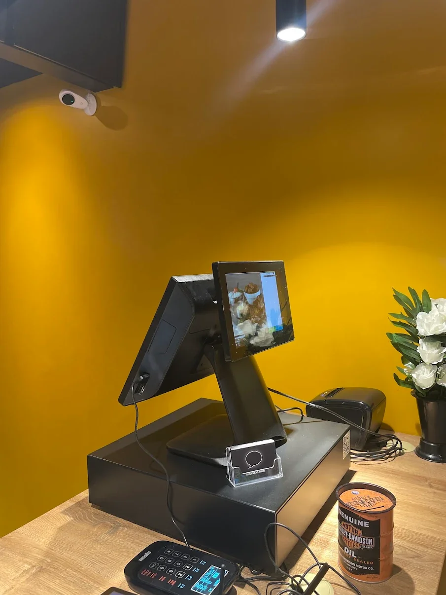 Caisse enregistreuse avec un écran tactile, une carte de fidélité, un paravent à fleurs blanches, et un fond jaune.