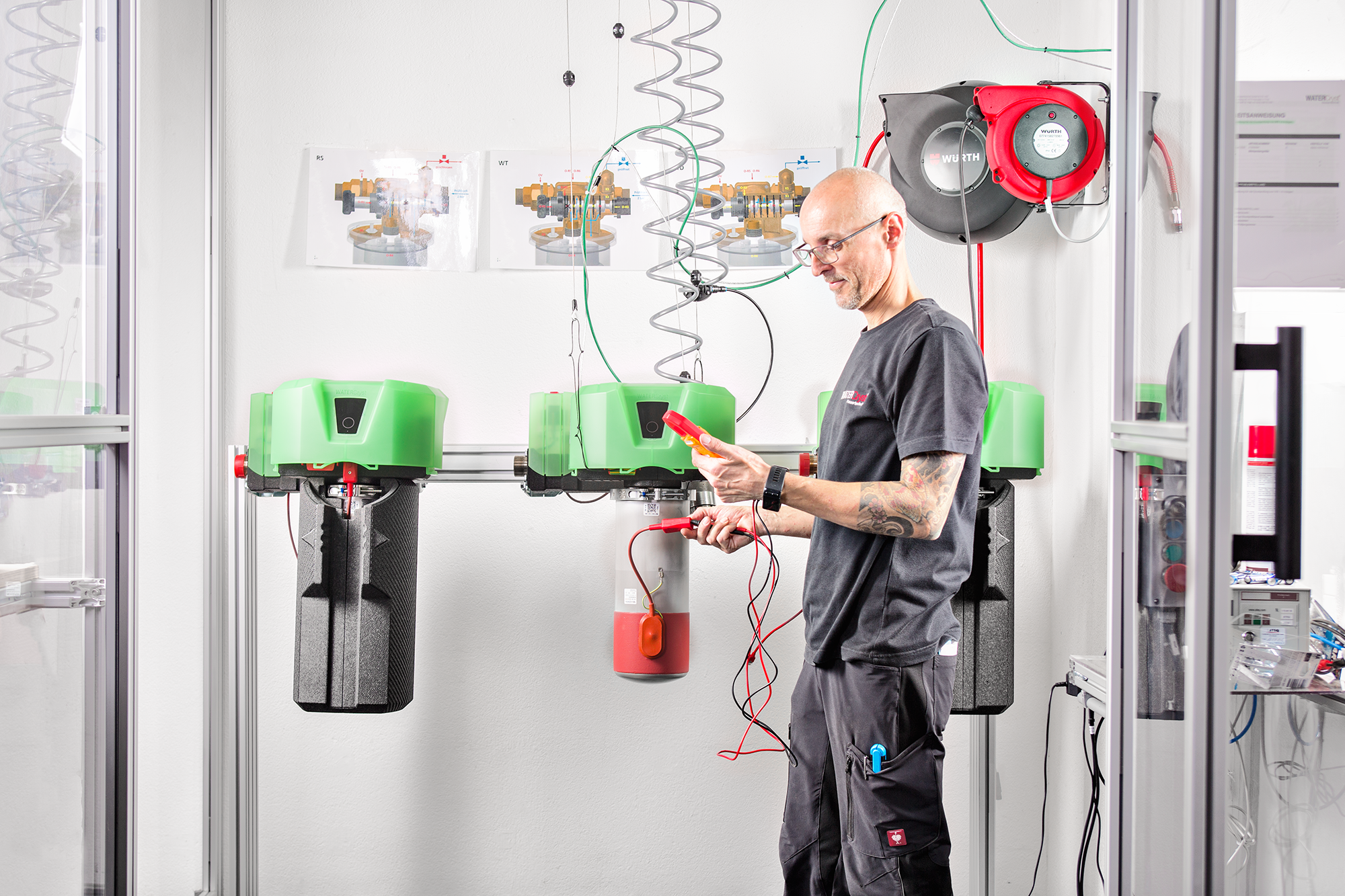 Mensch arbeitet in einem technischen Labor mit grünen Geräten und zeigt auf ein Elektrowerkzeug.