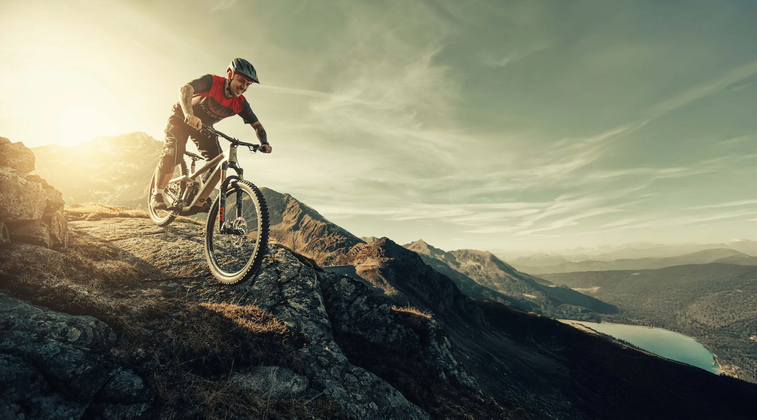 Ein Mann fährt mit einem Mountainbike auf einem felsigen Abhang in den Bergen bei Sonnenuntergang.