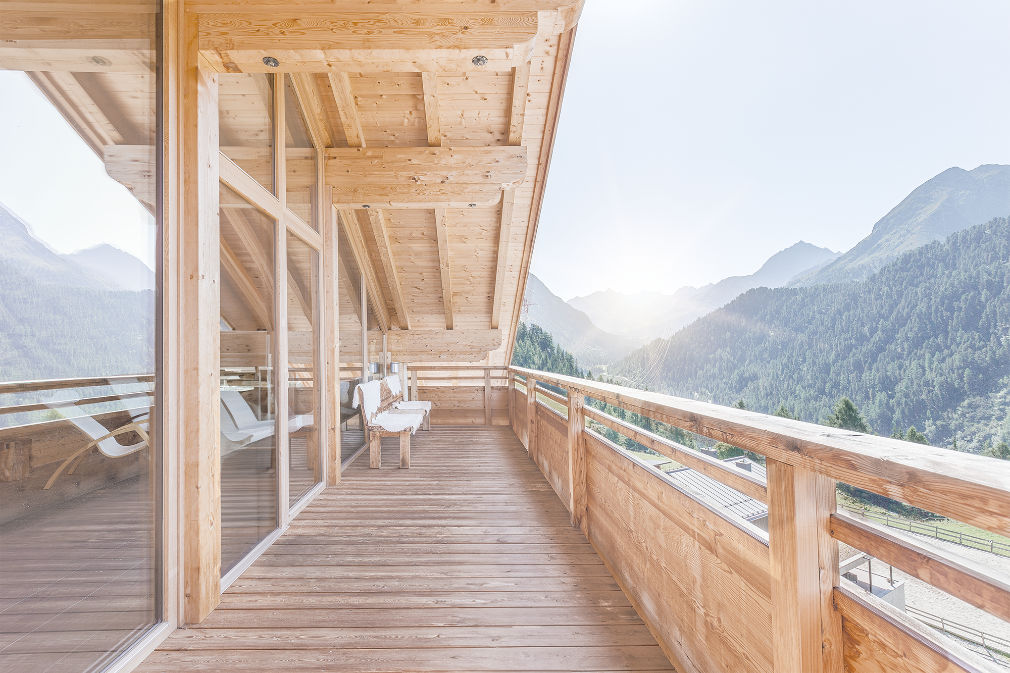 Holzverglaster Balkon mit Holzgeländer und Bergblick in den Alpen, sonniger Himmel, rustikale Sitzecke mit weißem Dekor.