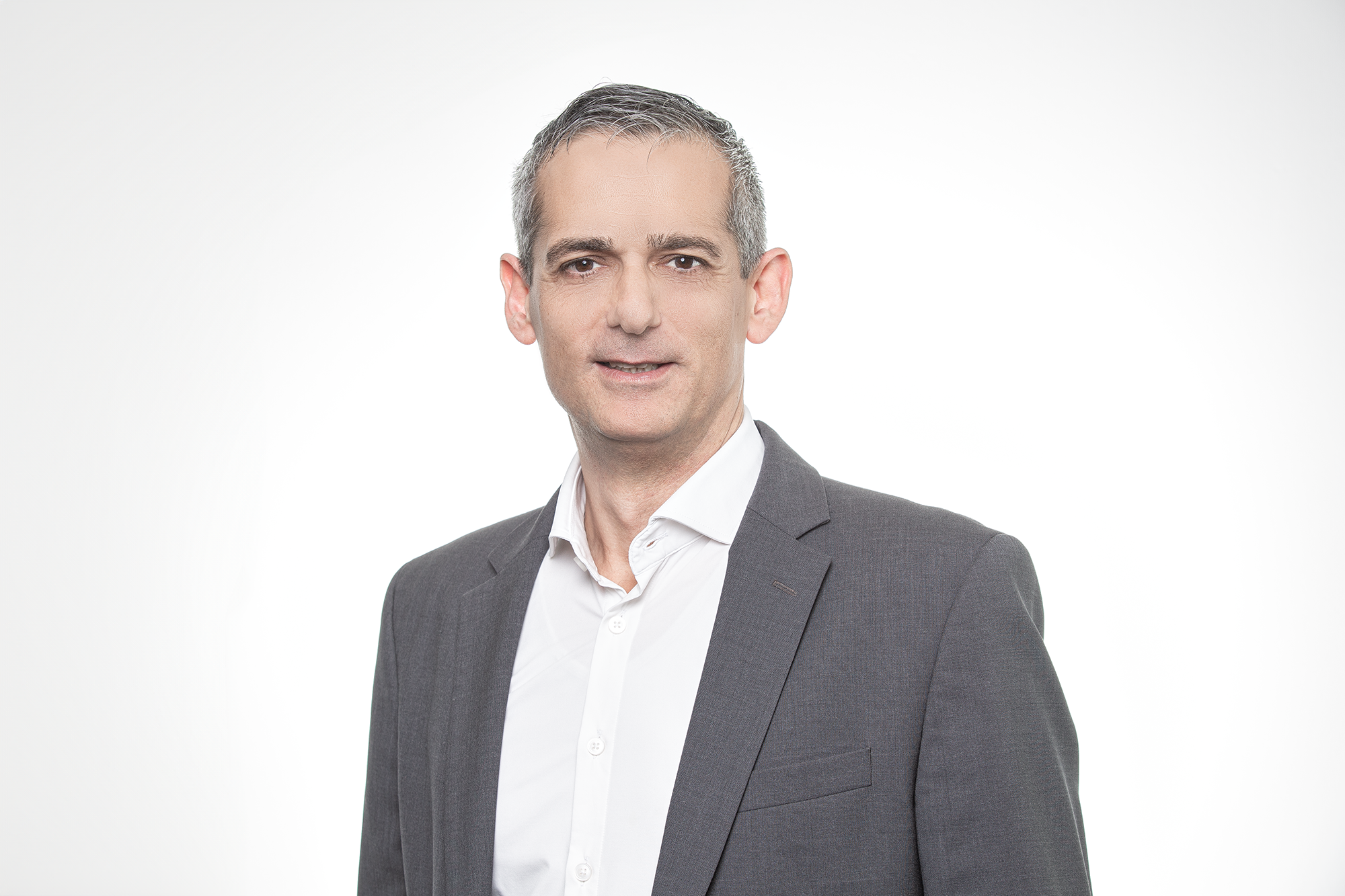 Ein professionell wirkender Mann in einem grauen Anzug und weißem Hemd steht vor einem weißen Hintergrund.