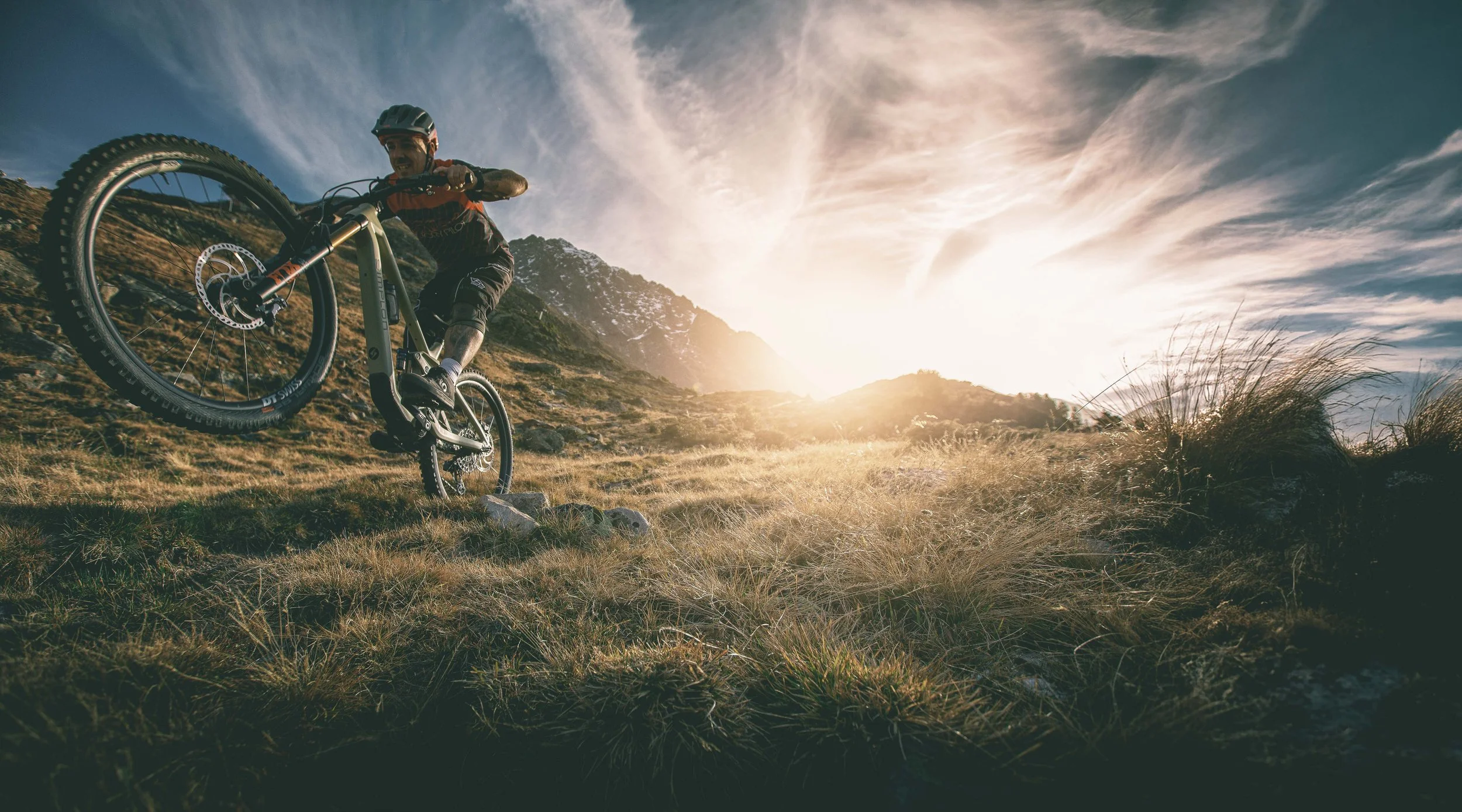 Ein Mountainbiker fährt auf einem unbefestigten Pfad in einer bergigen Landschaft während Sonnenuntergang.