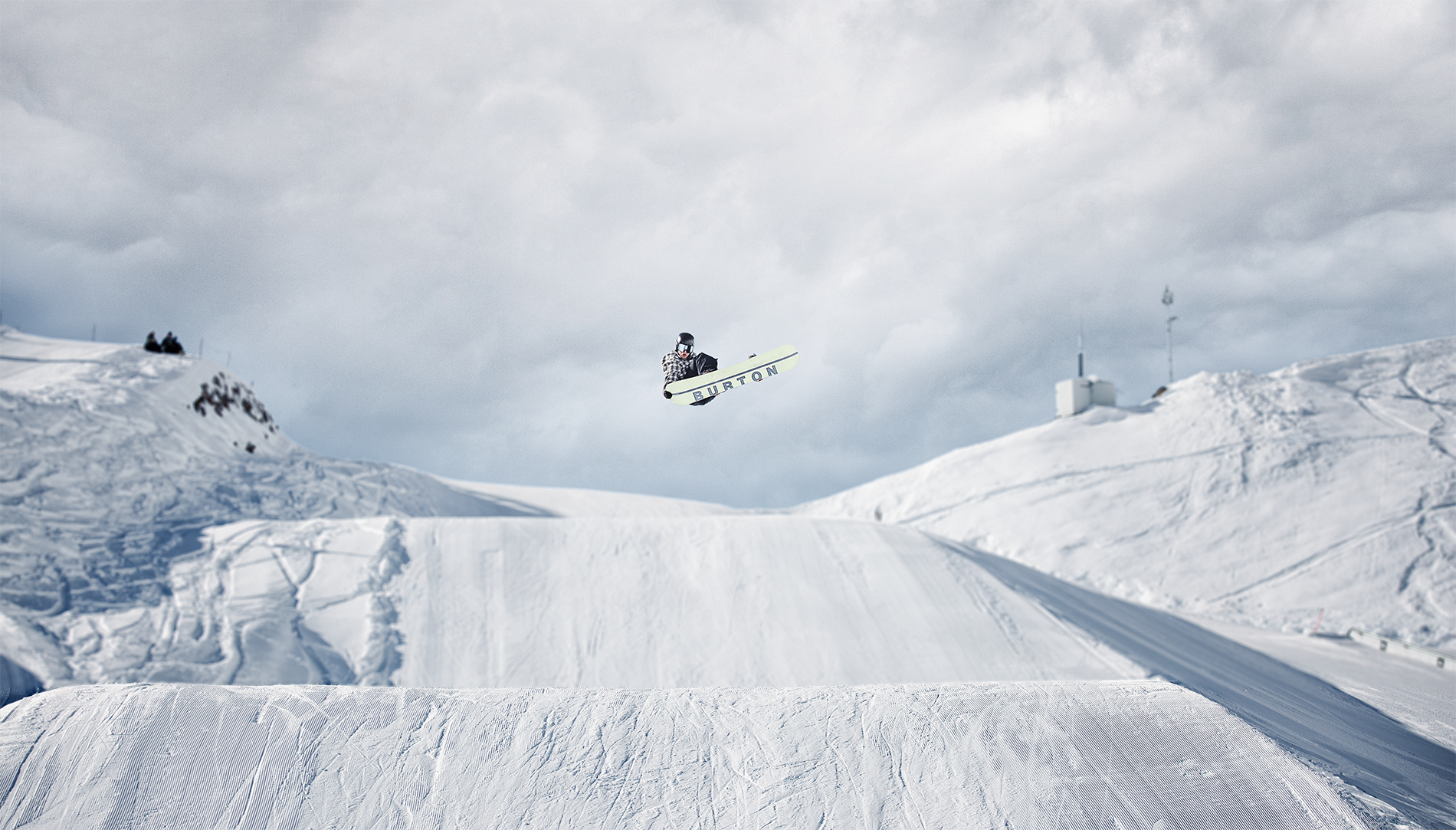 Skifahrer springt in der Luft auf einer verschneiten Piste bei bewölktem Himmel.
