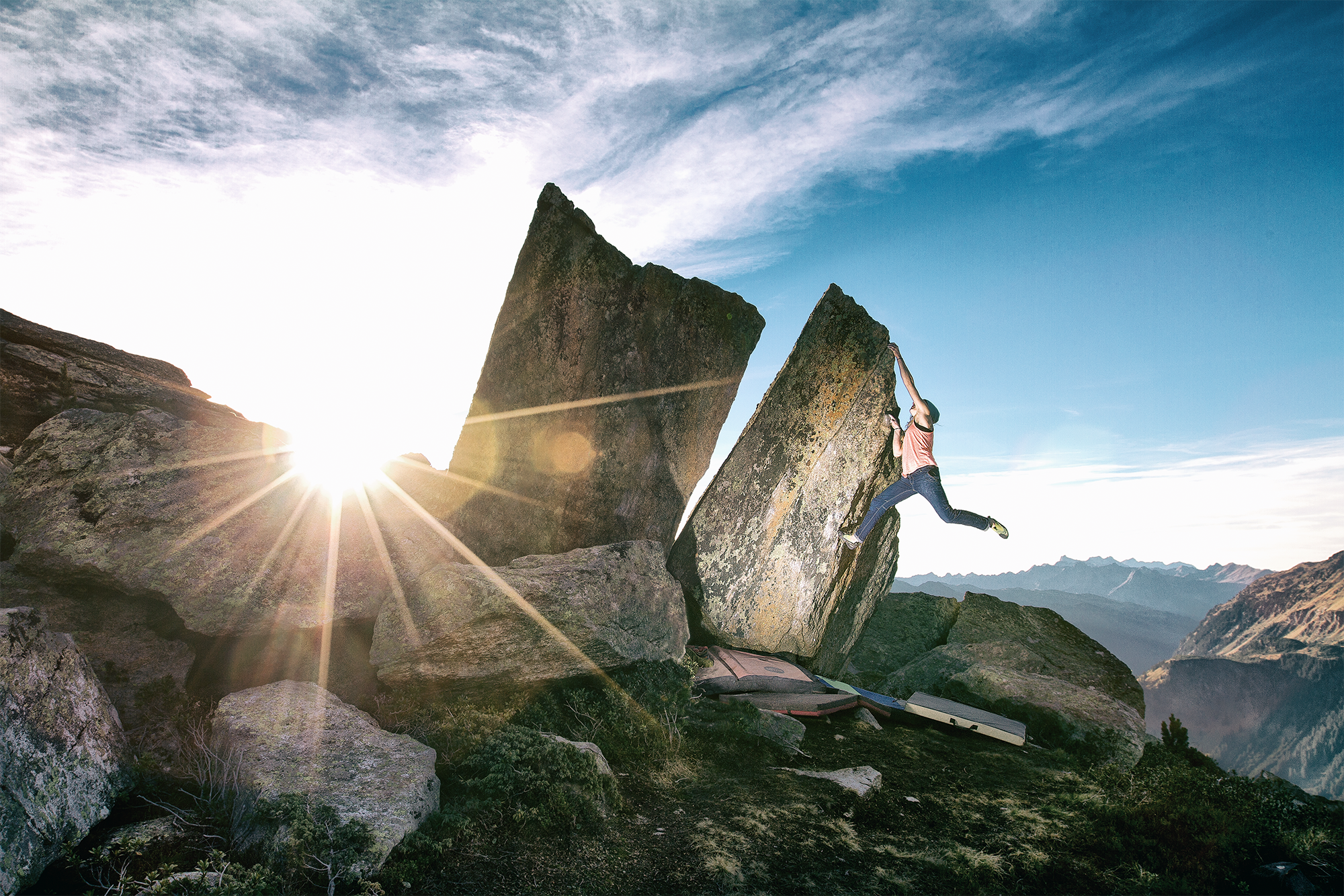 Klettererin beim Klettern an markiertem Felsen in bergiger Landschaft bei Sonnenuntergang.