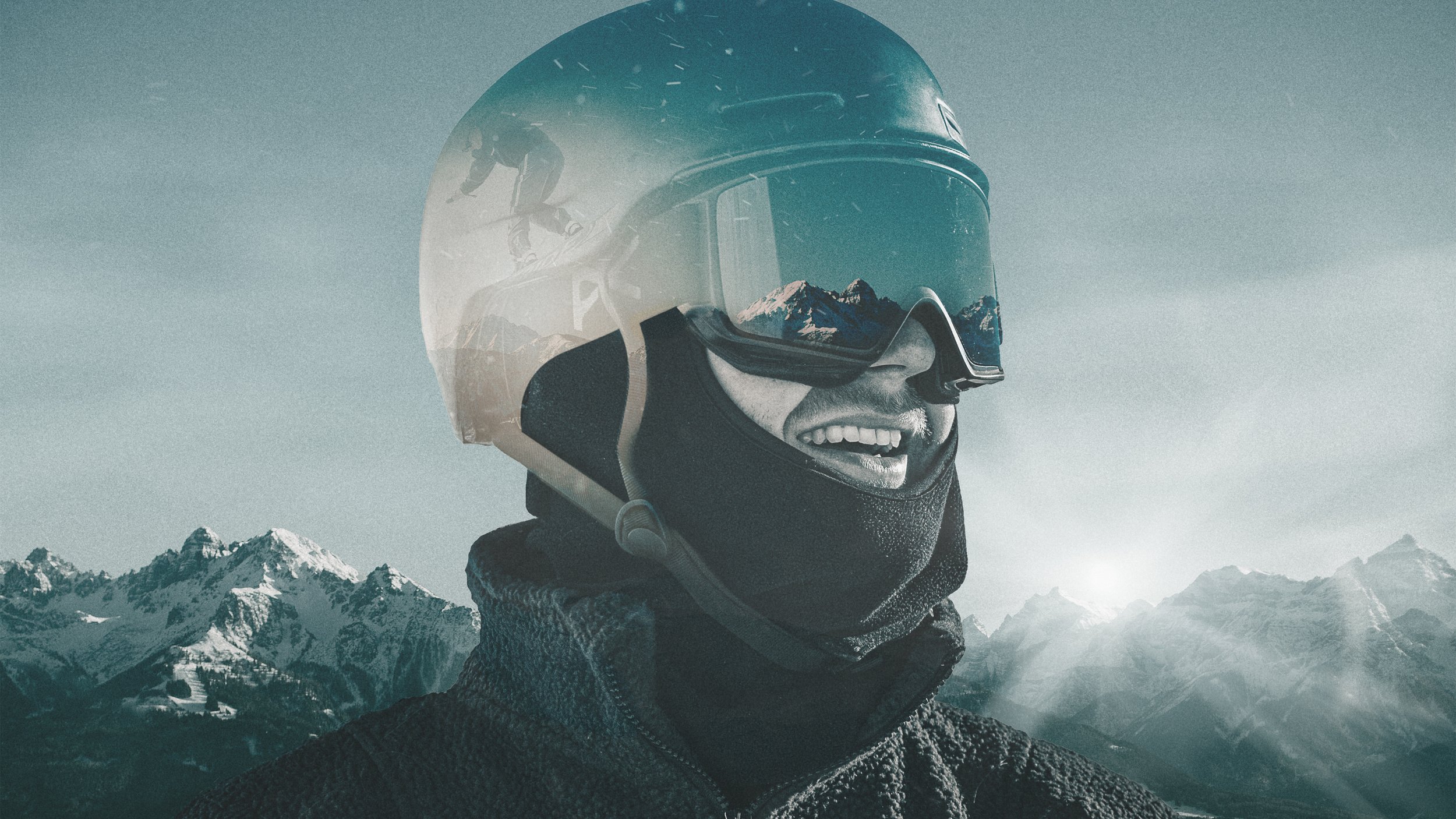 Ein Mann trägt einen schwarzen Helm mit visier, eine schwarze Halsmaske und einen schwarzen Pullover, vor einer Berglandschaft mit schneebedeckten Gipfeln, die im Sonnenlicht leuchten.