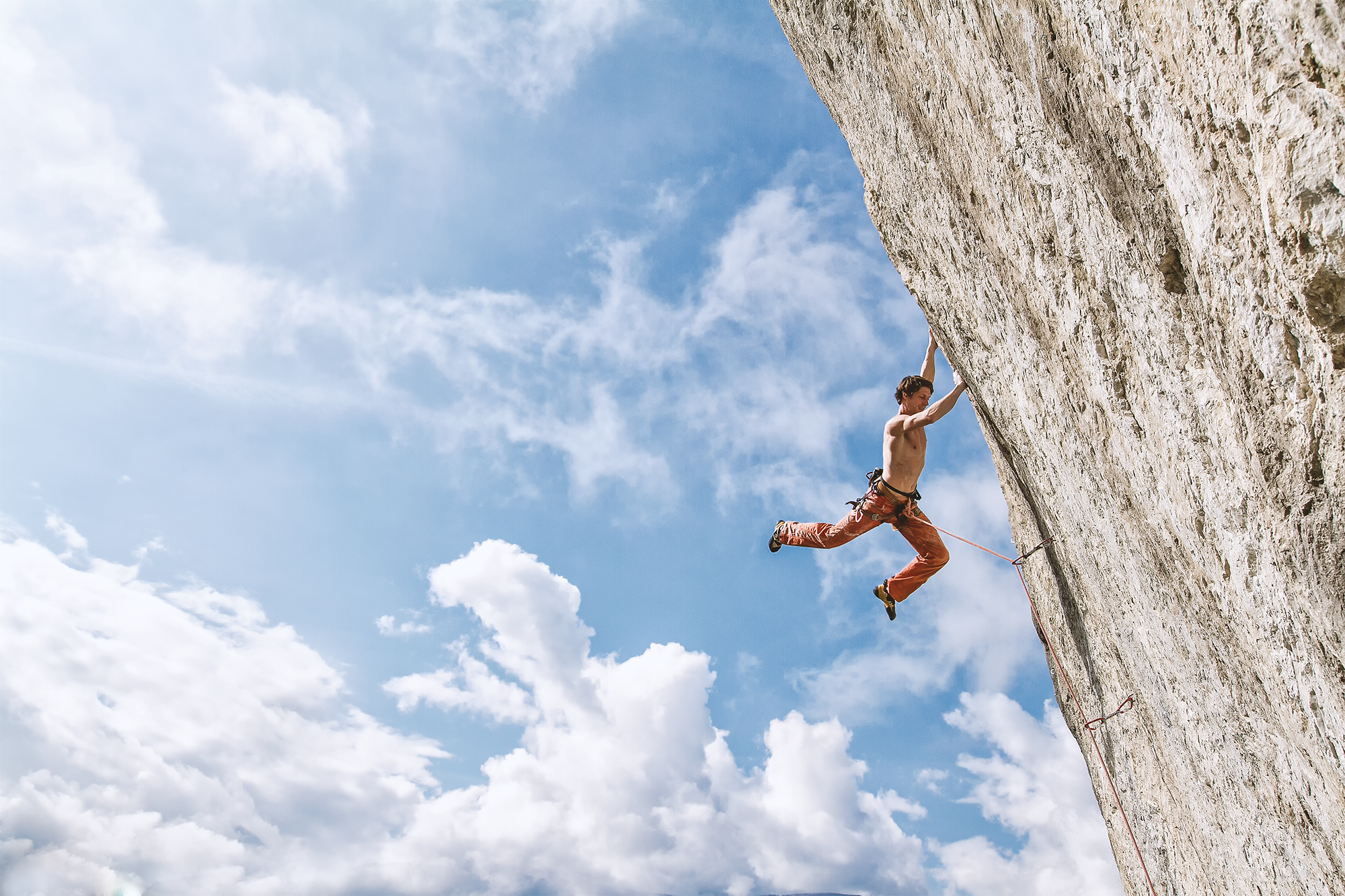 Felsenkletterer klettert an einer senkrechten Felswand im Freien, blauer Himmel mit Wolken im Hintergrund.