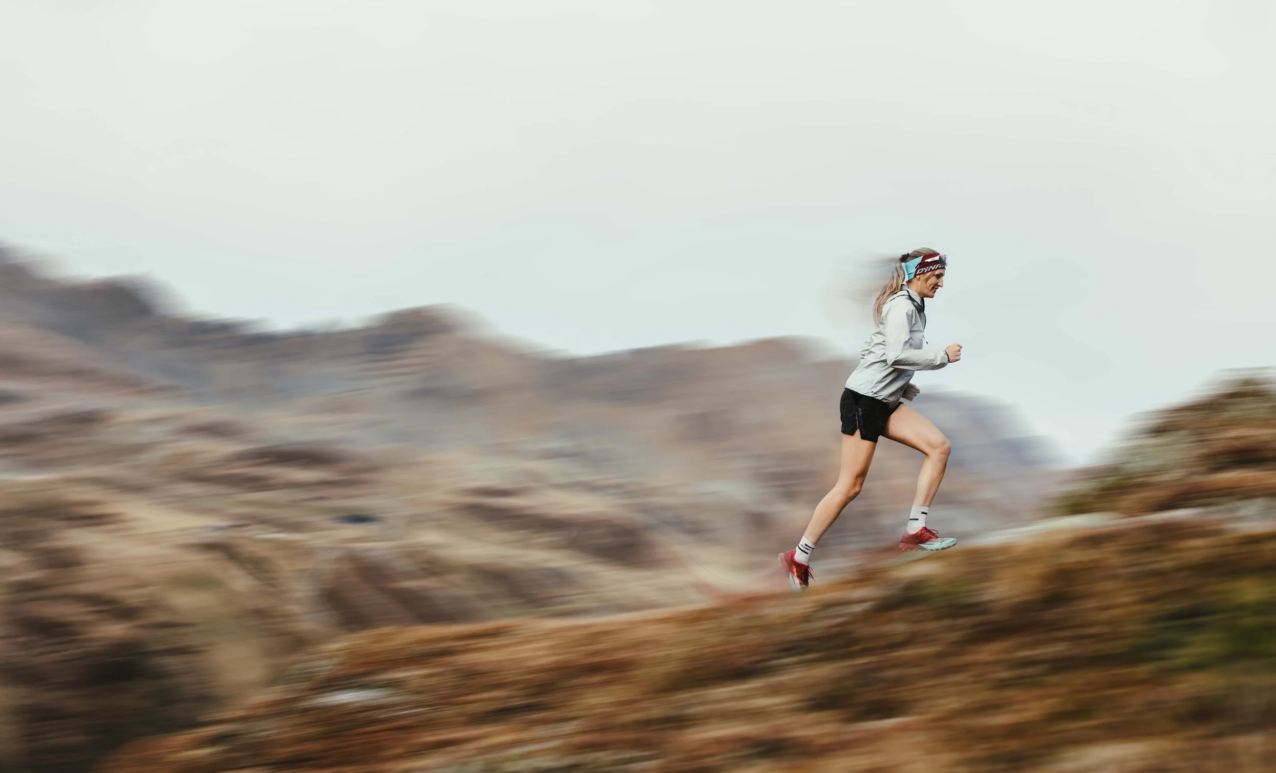Frau läuft beim Trailrunning in den Bergen, begleitet von Bewegung und Geschwindigkeit