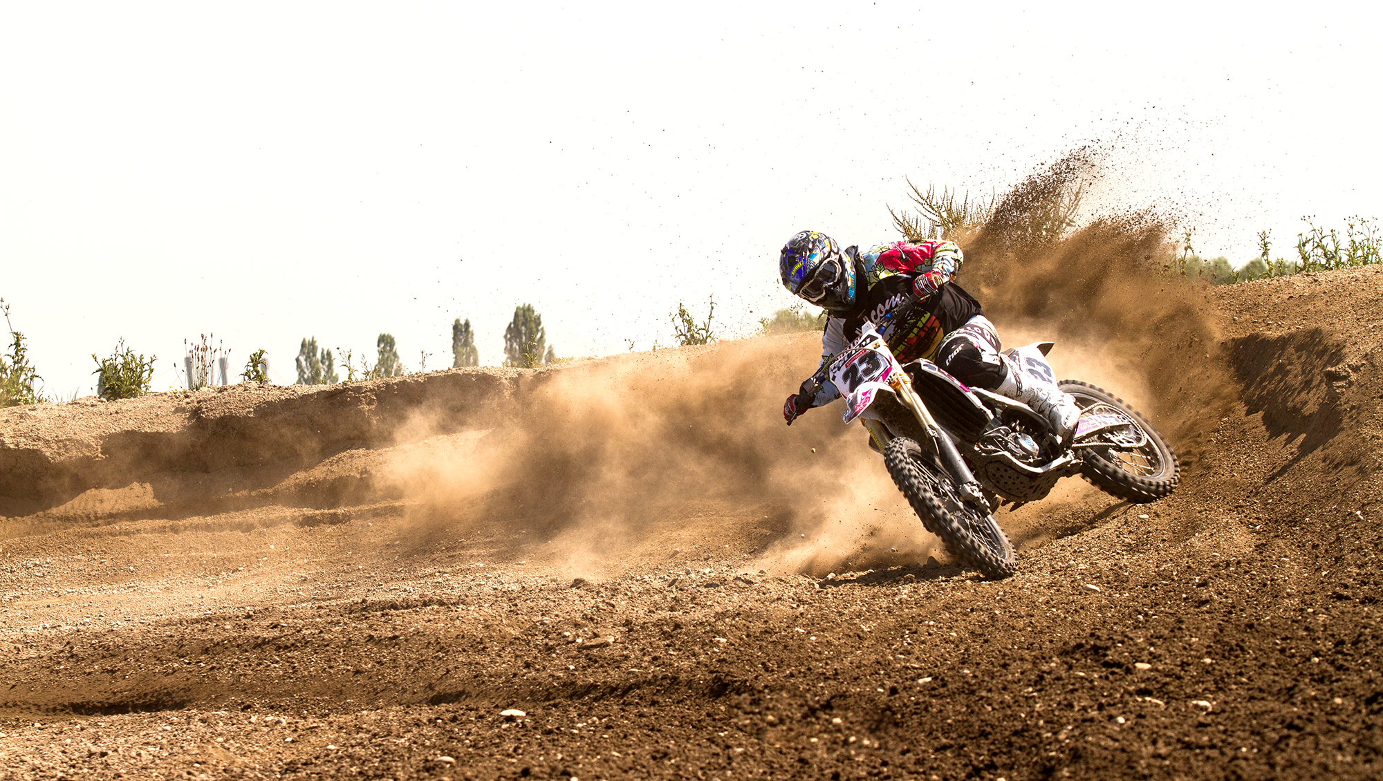 Motorradfahrer beim Crossrennen auf einer staubigen Piste, der seitlich in Kurve fährt.