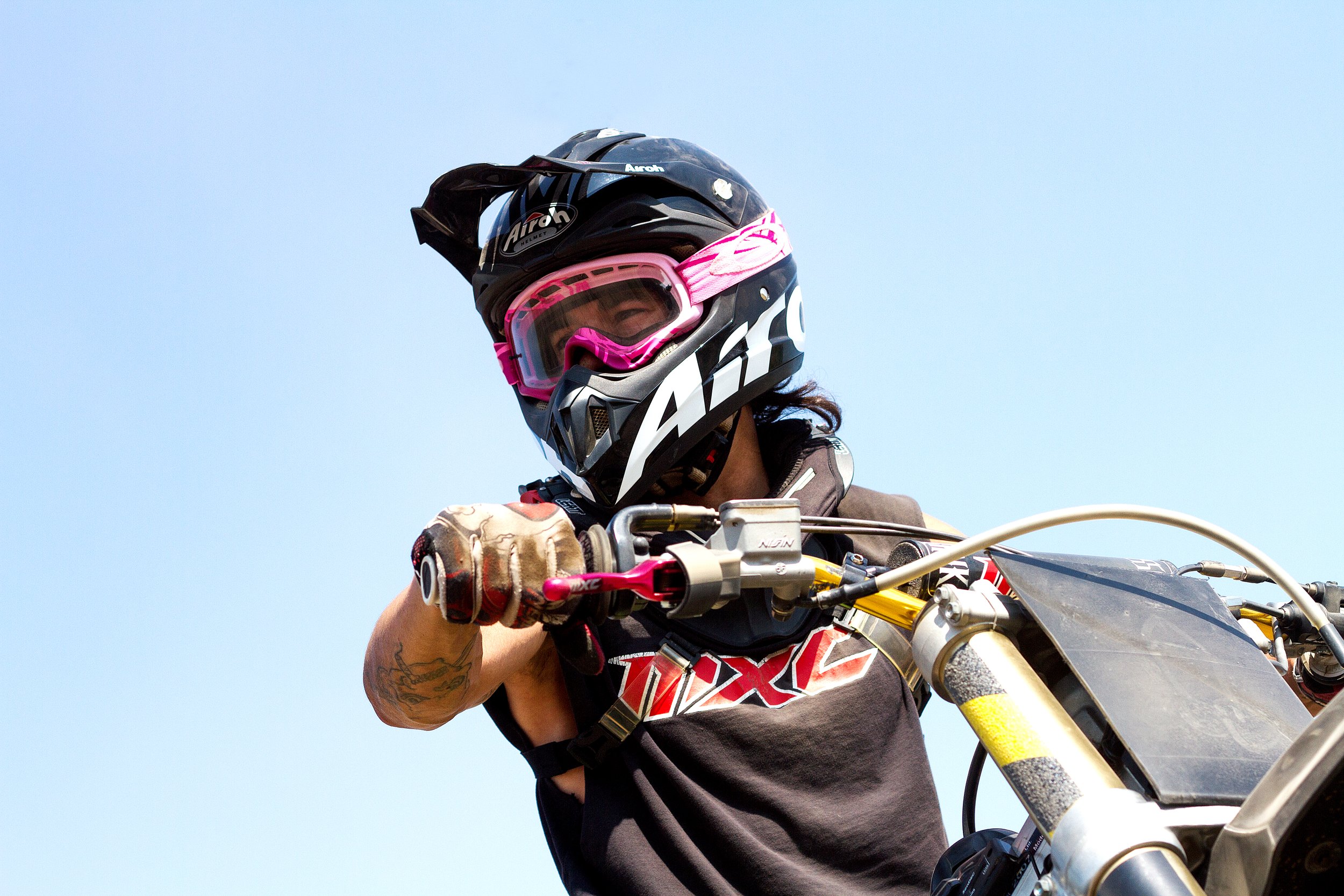 Motorradfahrer mit Helm und Schutzbrille auf einem Motorrad, beim Fahren im Freien bei blauem Himmel.