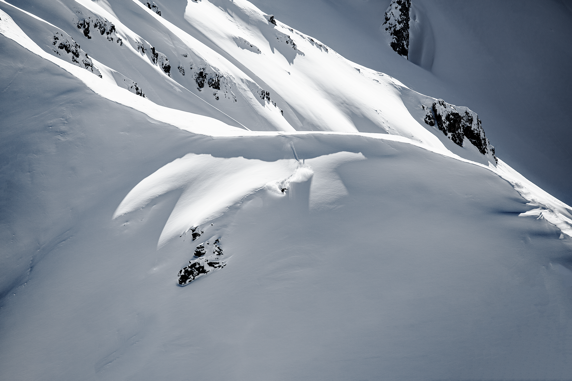 Ein Skifahrer fährt einen steilen, schneebedeckten Hang in den Bergen hinunter.