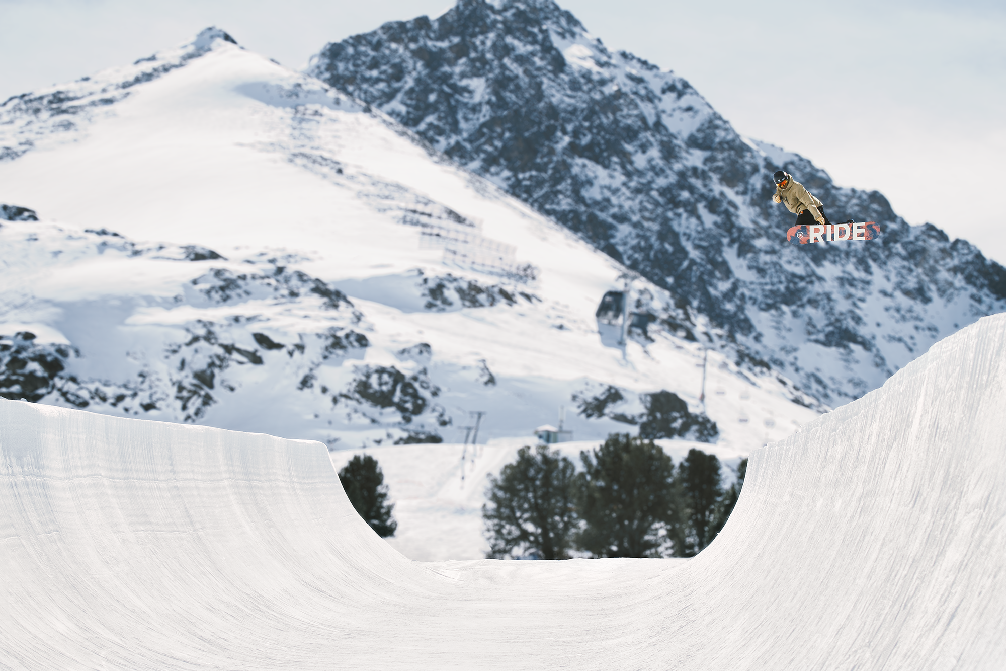 Ein Skifahrer springt von einem Snowboard im Skisprung in einer verschneiten Berglandschaft.