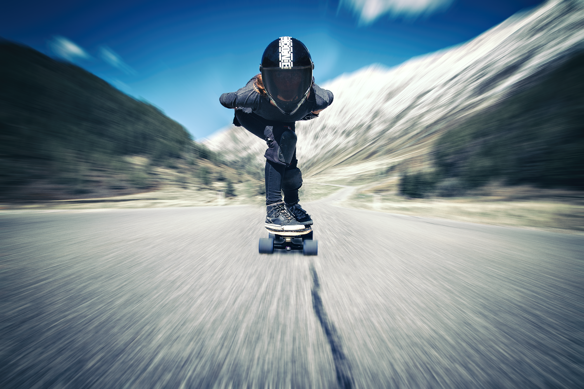 Skateboarder auf einer Straße in den Bergen bei sonnigem Wetter, Blick nach vorne, Bewegungseffekt