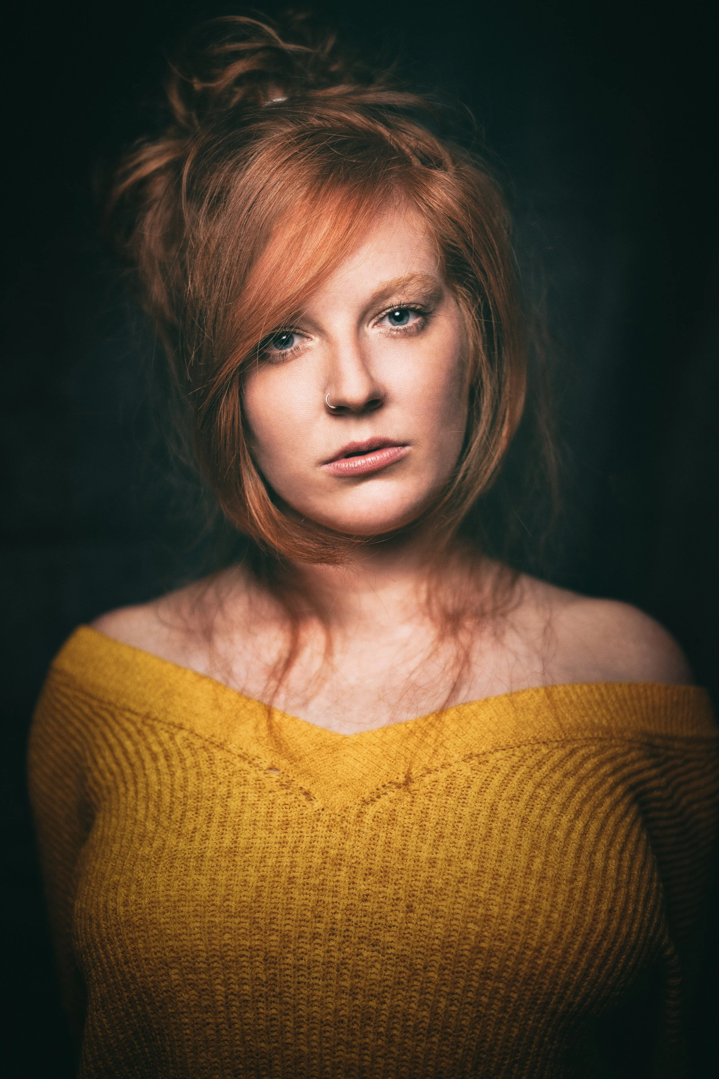 Porträt einer jungen Frau mit roten Haaren, blauen Augen, trug ein gelbes Oberteil, auf dunklem Hintergrund.