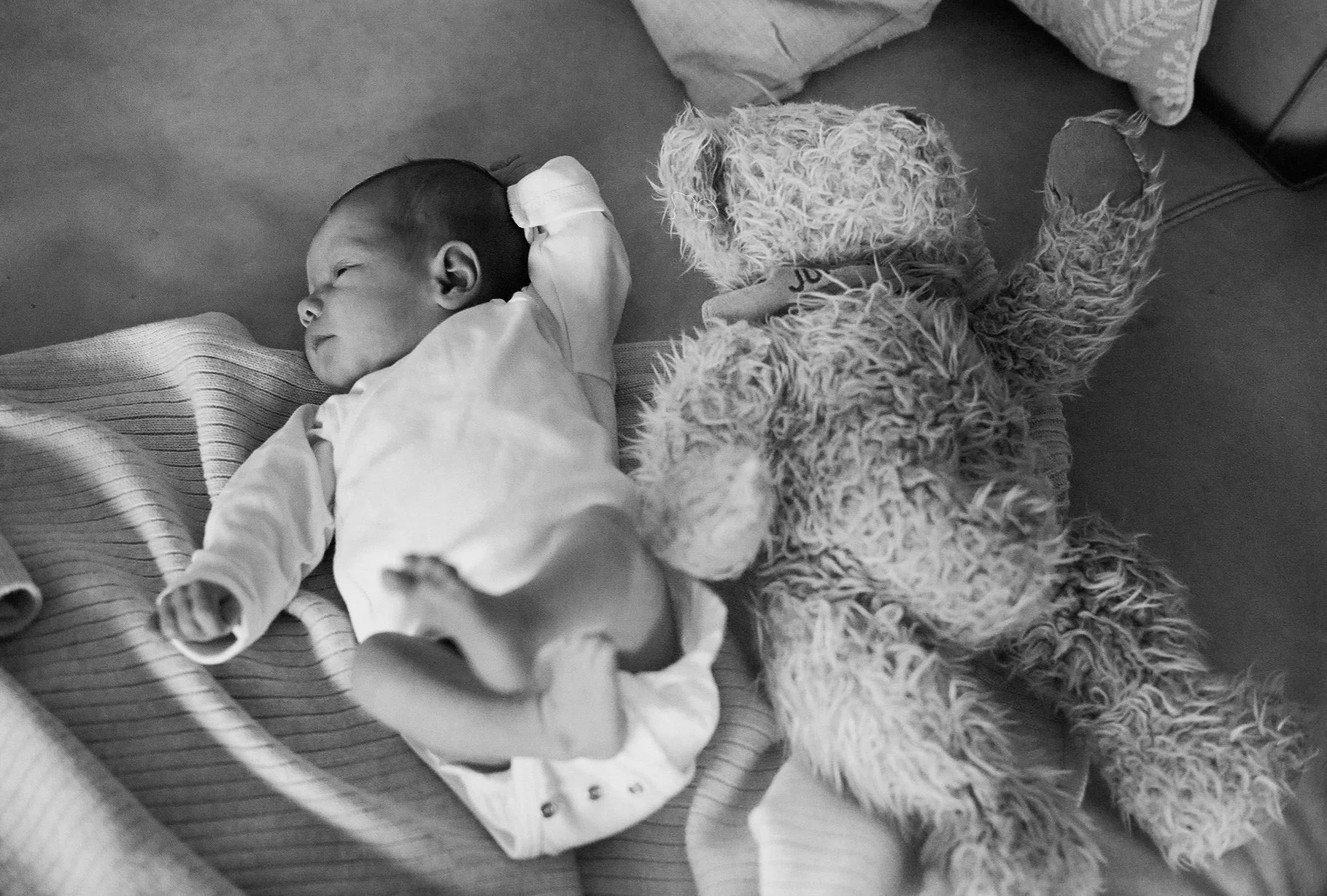 Ein schlafender kleiner Junge mit einem Teddybär auf einem Bett. analoge Babyfotographie