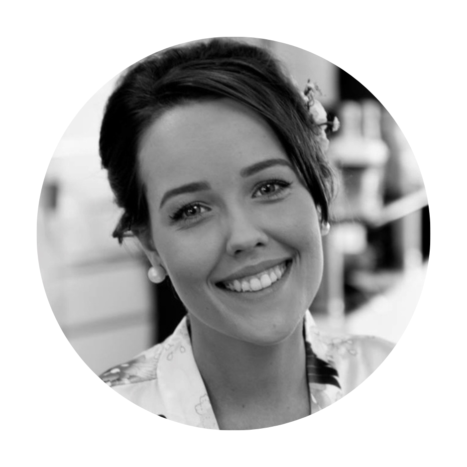 Black and white portrait of a smiling woman with pearl earrings and a floral blouse, in an indoor setting.