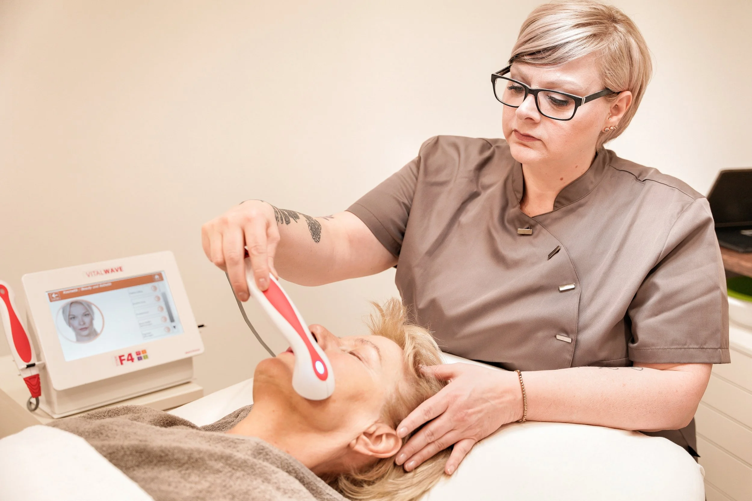 Ärztin führt eine Gesichtsbehandlung mit einem medizinischen Gerät an einer älteren Patientin durch, die auf einer Liege liegt.