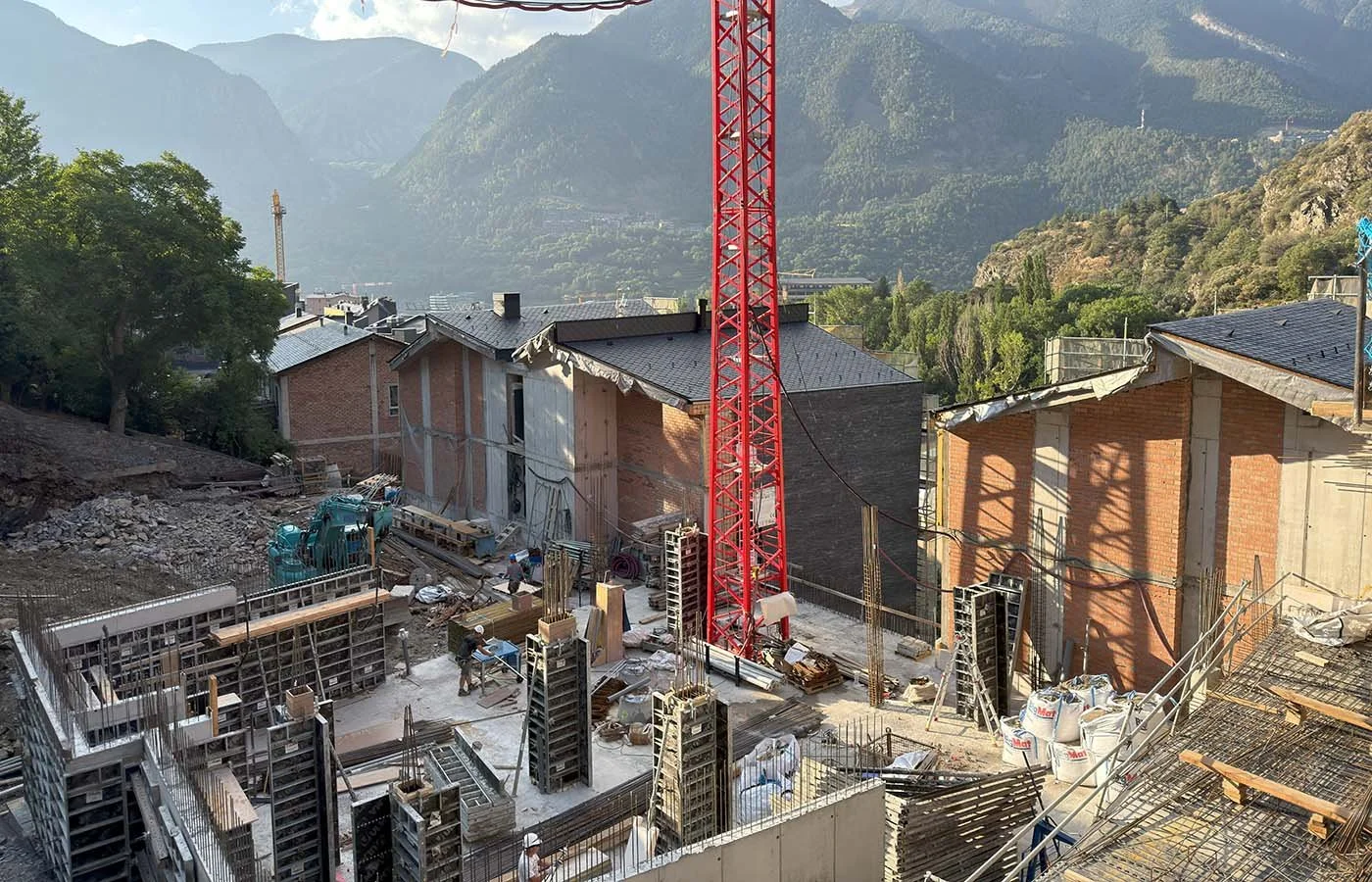 Obra en construcción con maquinaria pesada y trabajadores en un sitio rodeado de montañas.