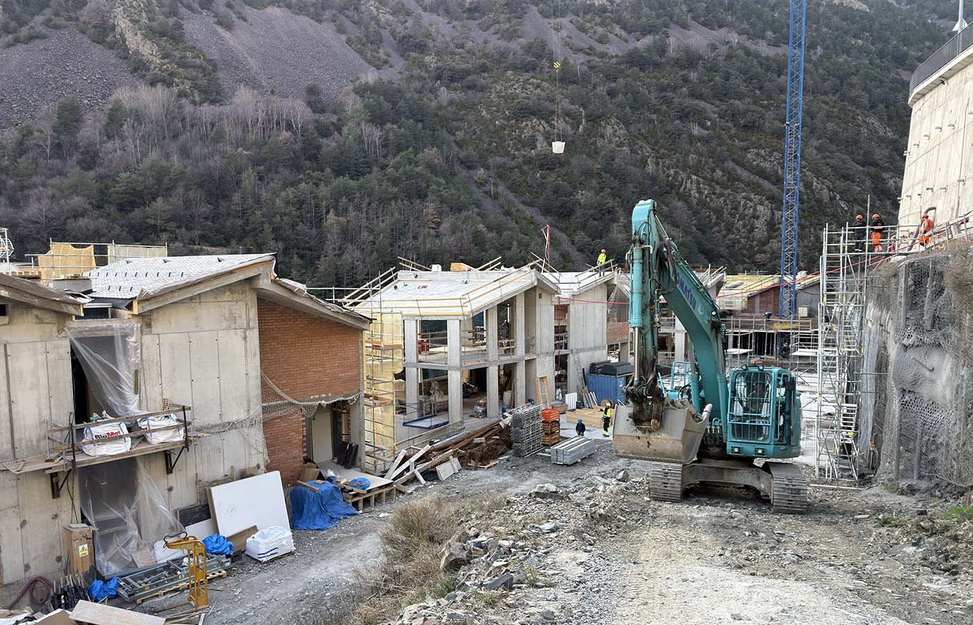 Obra en construcción con maquinaria pesada y trabajadores en un sitio rodeado de montañas.