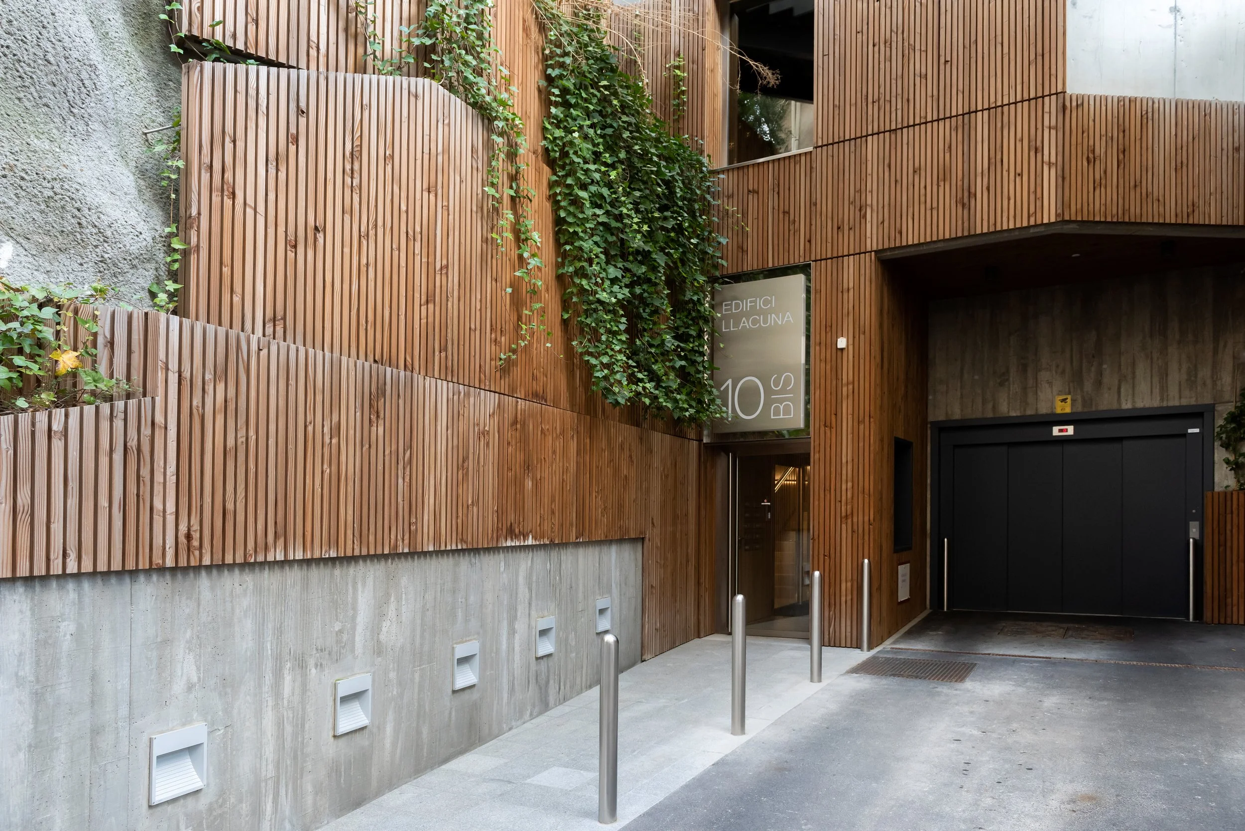 Entrada de l'edifici La Llacuna, amb recobriment de fusta i vegetació decorativa a la façana.