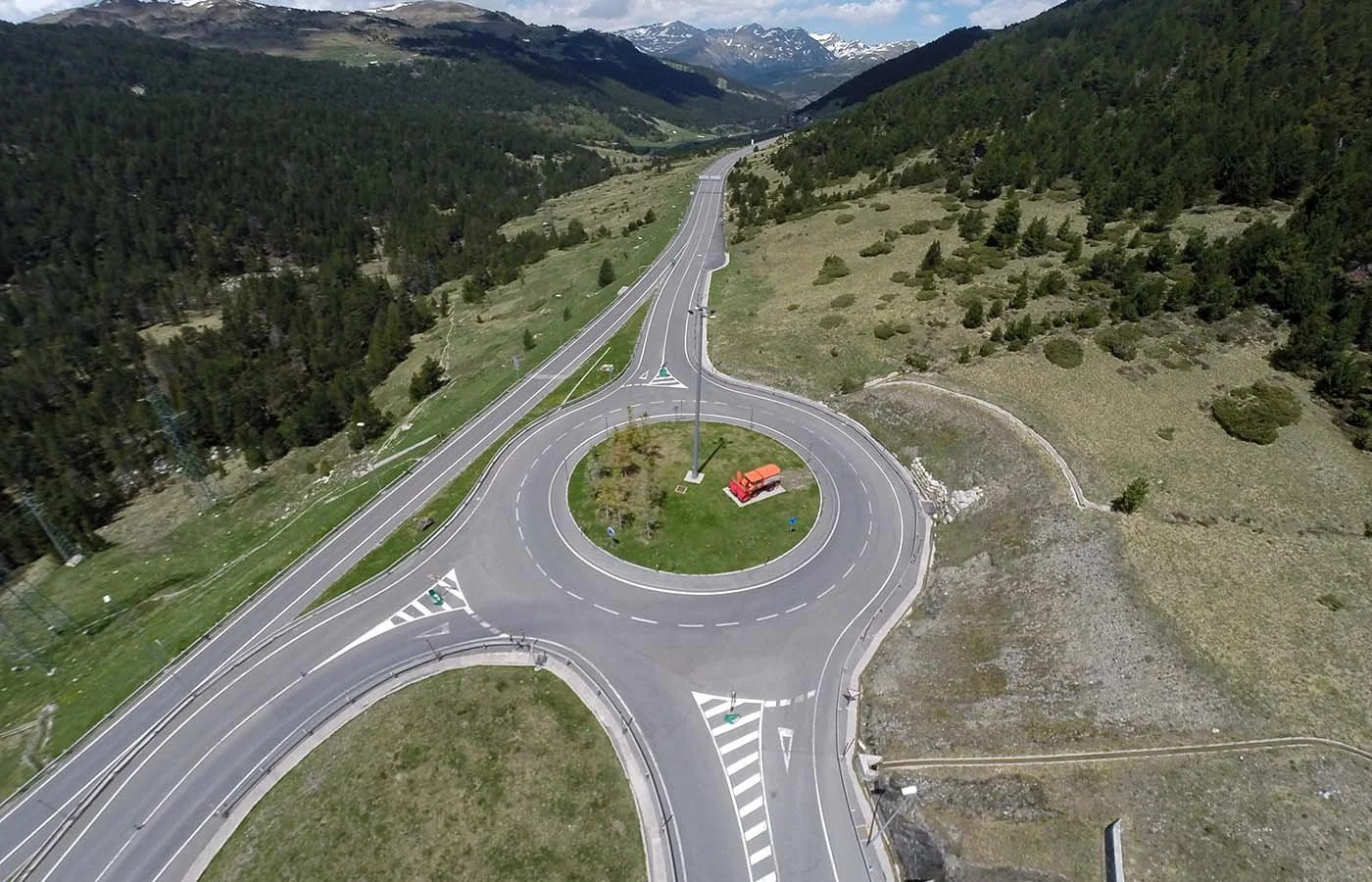 Vista aérea de una rotonda en un área rural rodeada de montañas y bosques, con varias carreteras que la atraviesan.