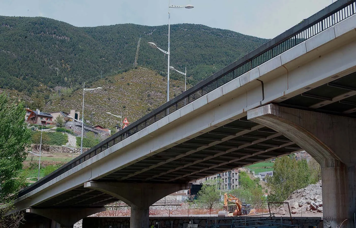 Puente de concreto sobre un río en un paisaje montañoso con casas y árboles