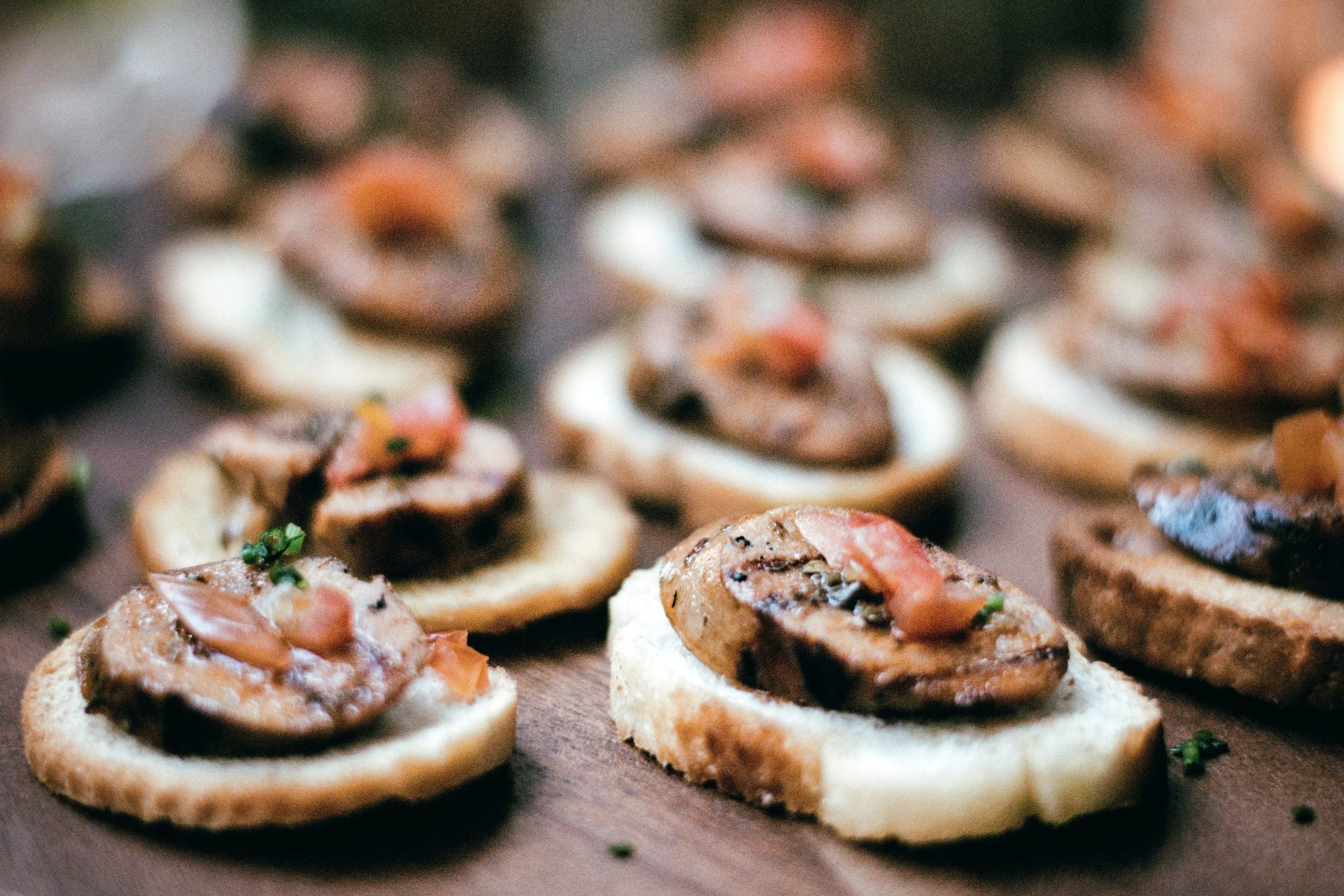 Close-up of multiple pieces of toast with meat, tomato, and herbs on a wooden surface.