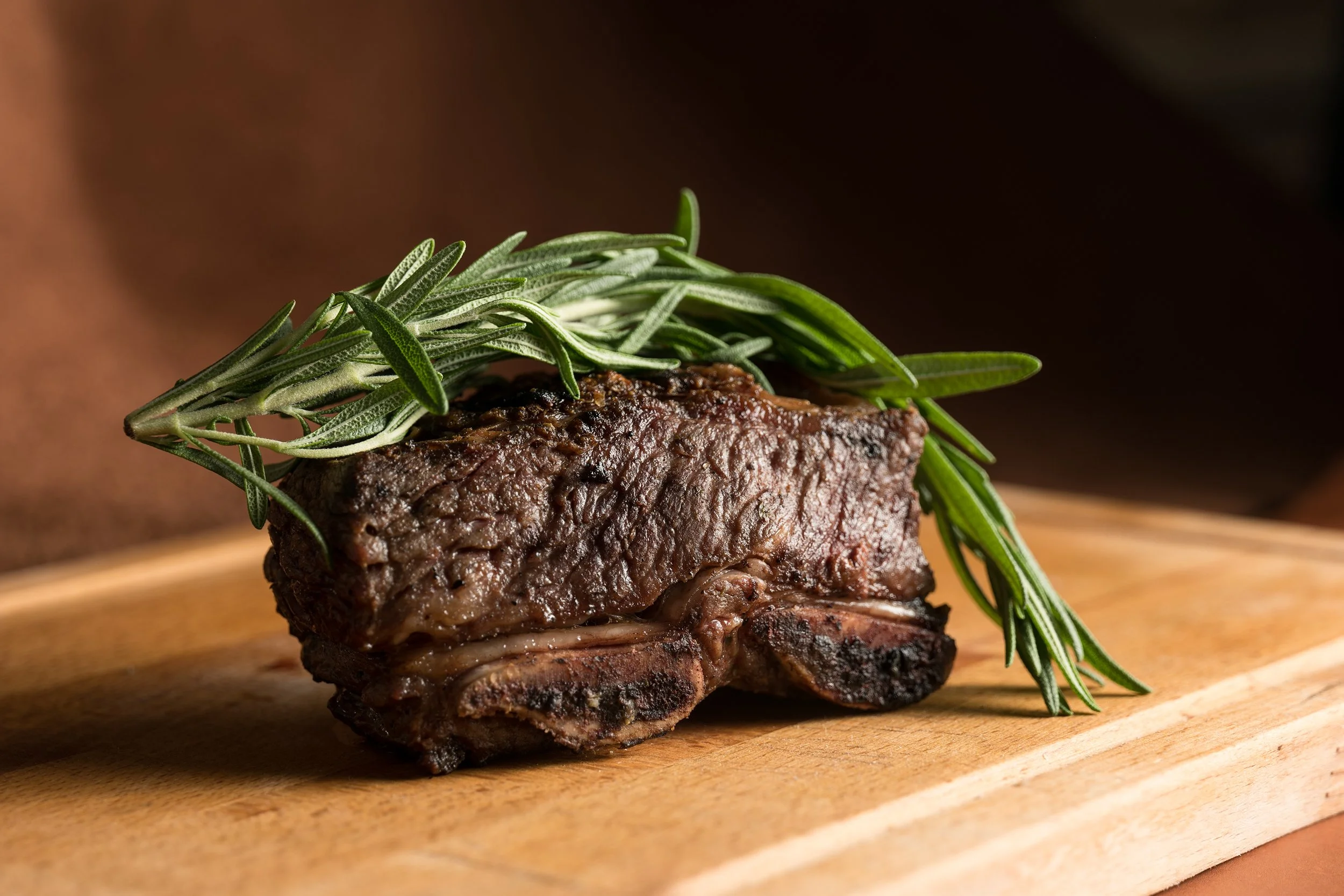 A cooked steak garnished with fresh rosemary on a wooden cutting board.