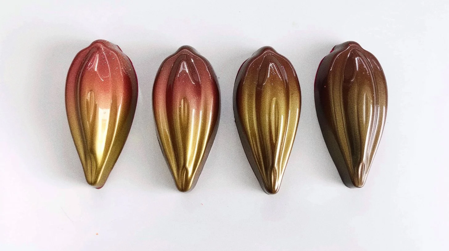 Vier kunstvolle Schokoladen in Blütenform mit gold, braun und rosa Mustern, auf weißem Hintergrund