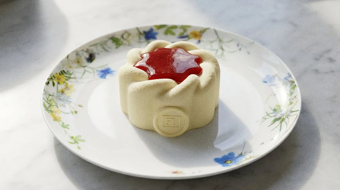 Ein petit fours mit weißem Schokoladenmantel und roter Fruchtsoße auf einem weißen Teller mit Blumenmuster.