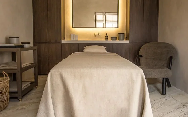 Schlafzimmer mit Einzelbett, grauem Sessel, Holz- und beigefarbenem Dekor, Wandspiegel mit Beleuchtung.