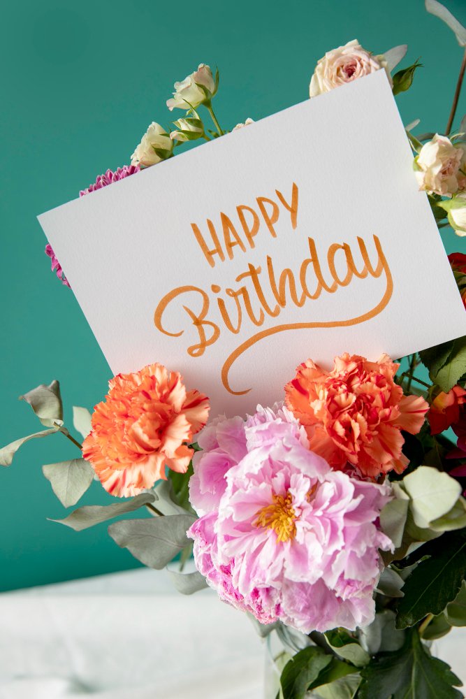 Blumenstrauß mit pinken, weißen und orangefarbenen Blumen, mit Karte, die 'HAPPY Birthday' schreibt.