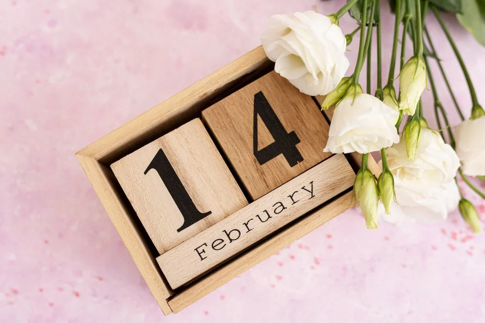 Holzkachel mit Datum 1. Februar 4. und weißen Blumen auf rosa Hintergrund.