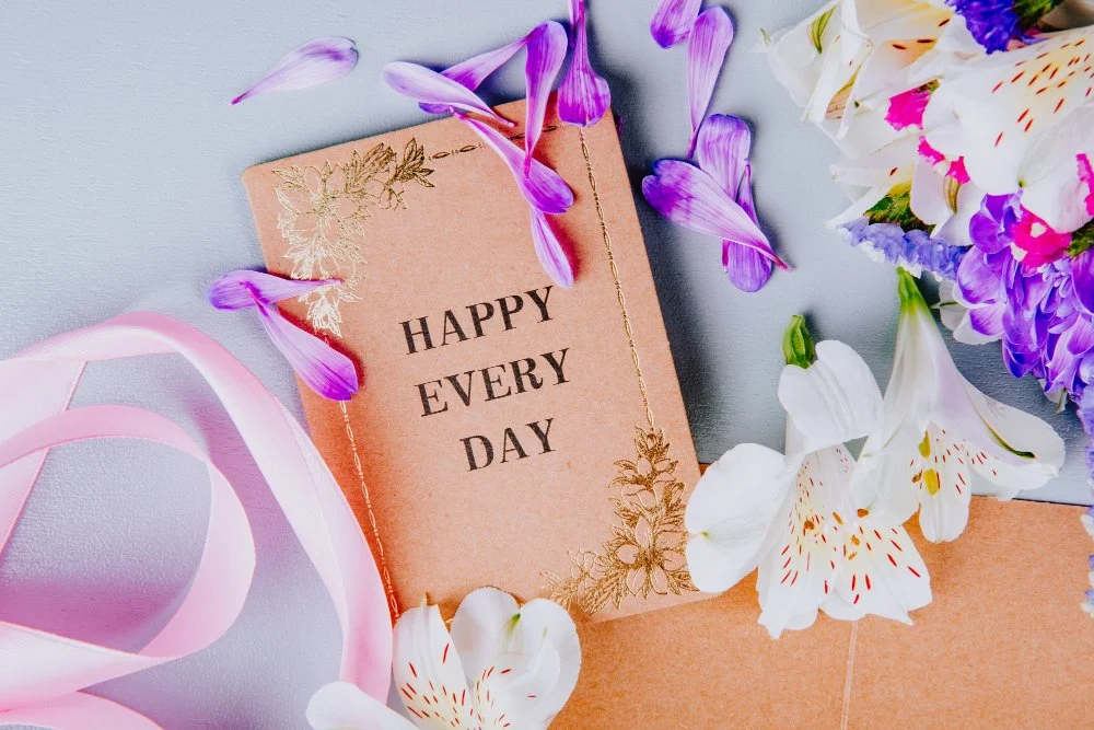 Grußkarte mit der Aufschrift "Happy Every Day" umgeben von Blumen und rosa Schleifen.